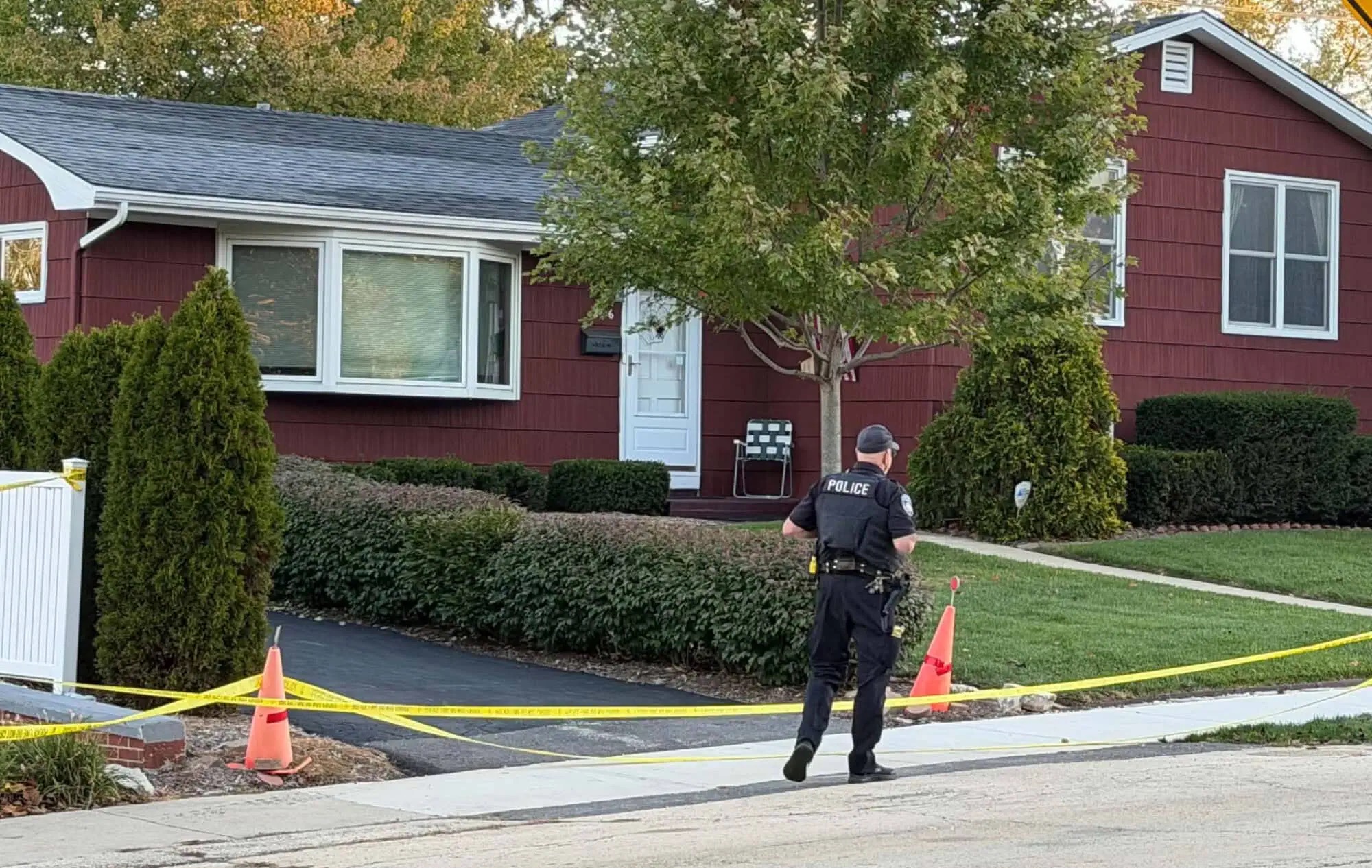 A Mundelein police officer walks toward the Schmidt family home, where yellow crime scene tape and traffic cones block the driveway as investigators examine the property. | Source: Nick Rusin / Lake & McHenry County Scanner.