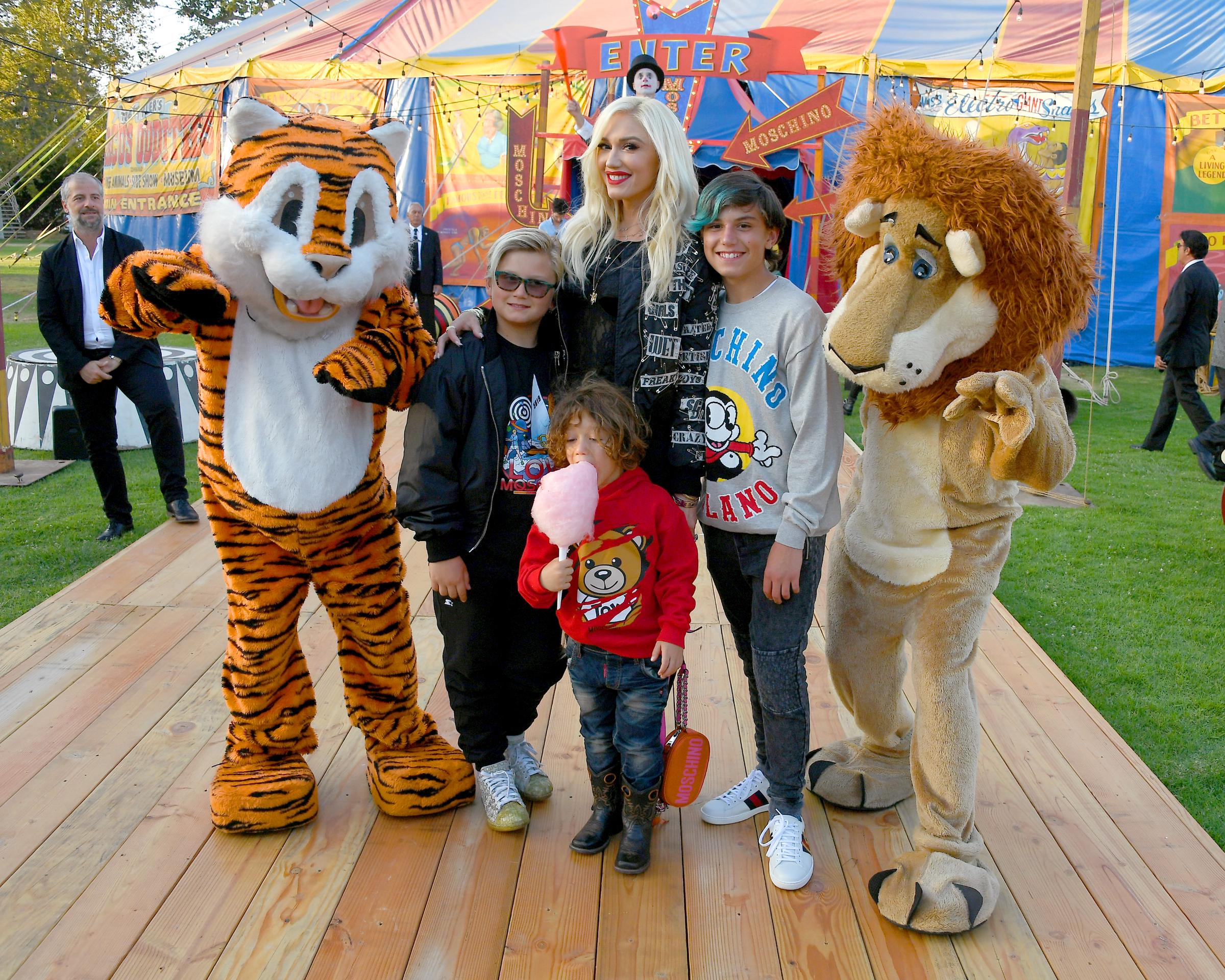 Nine-year-old Zuma Rossdale channeled effortless rockstar energy with his stylish blonde hair, sleek black bomber jacket, and cool sunglasses alongside Gwen Stefani, Apollo Bowie Rossdale, and Kingston Rossdale. At this event, they posed with costumed performers during the Moschino Spring/Summer 19 Menswear and Women's Resort Collection at Los Angeles Equestrian Center on June 8, 2018, in Burbank, California. | Source: Getty Images
