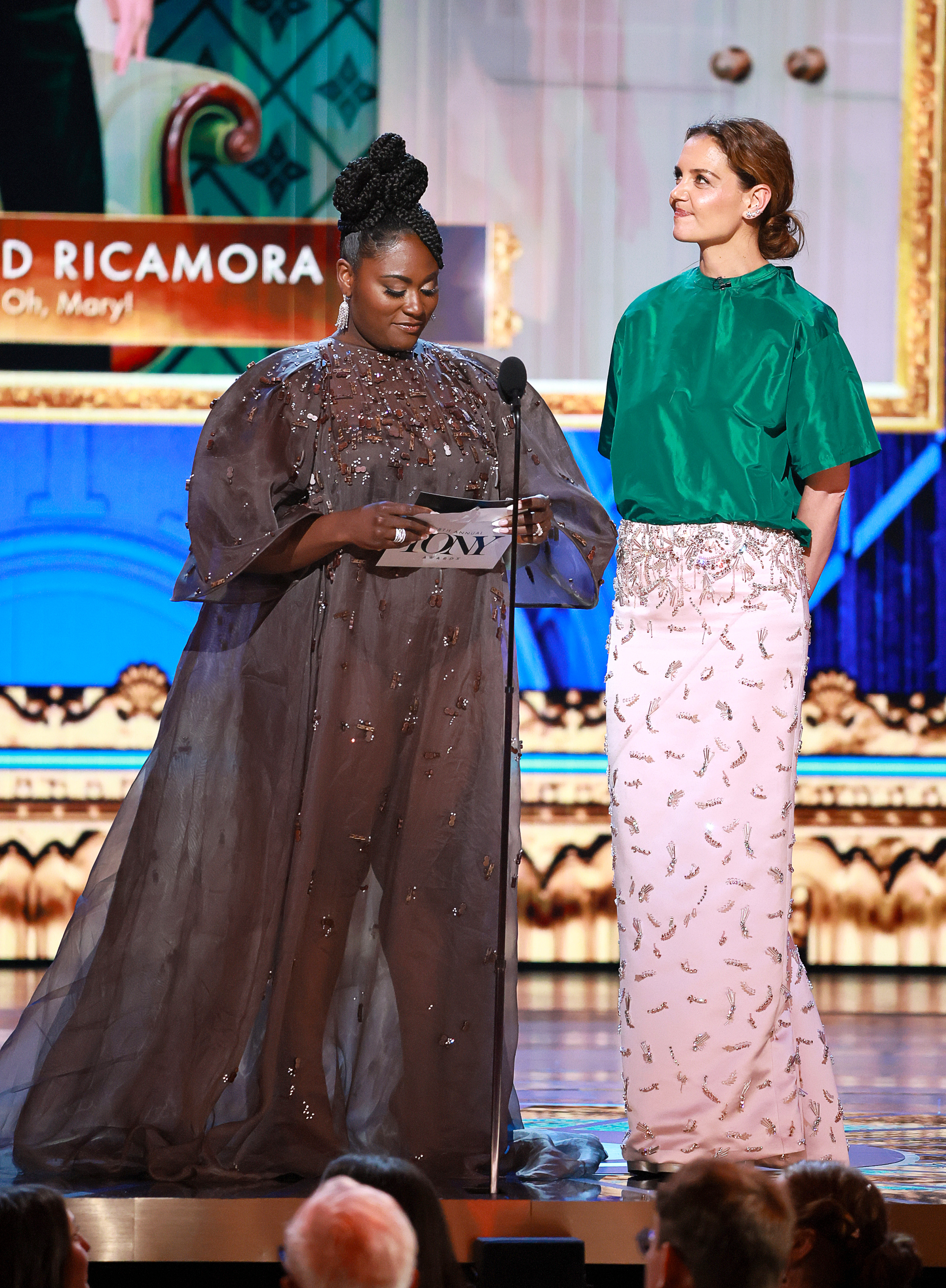In a vibrant contrast of green and soft pink, Katie Holmes stands beside Danielle Brooks as they present an award at the 2025 Tonys, capturing the spotlight with color and confidence.