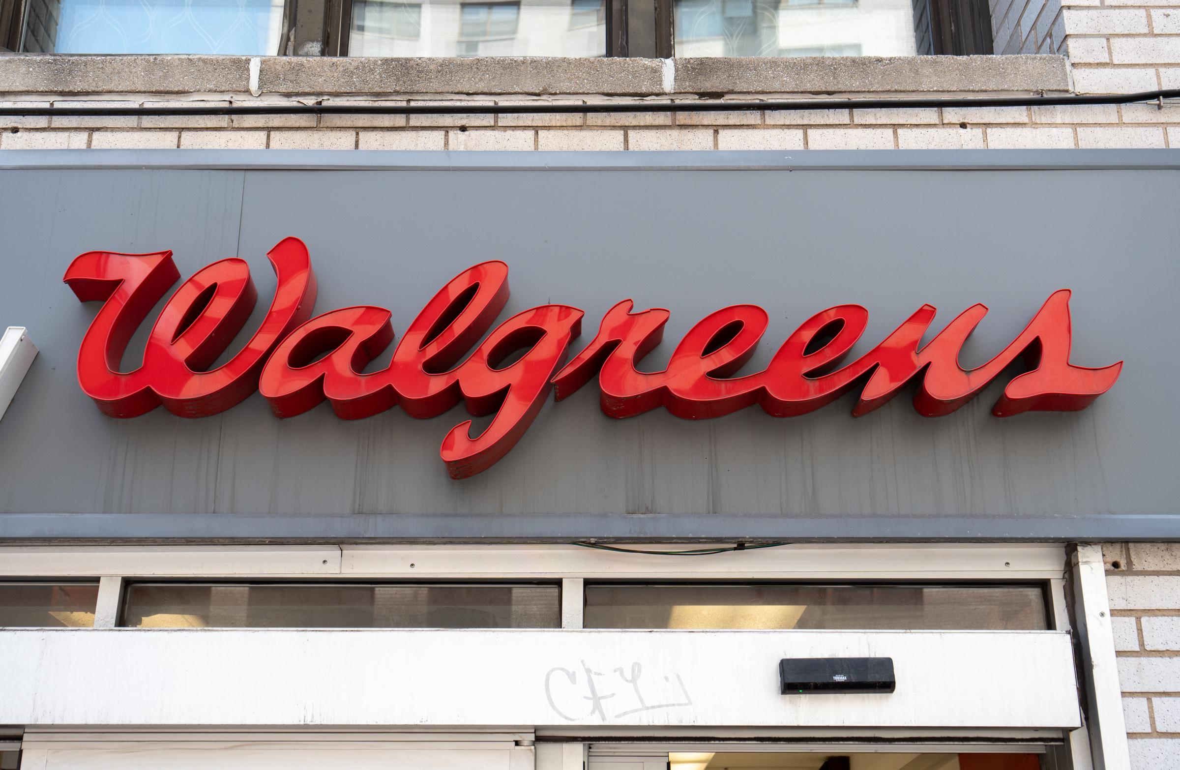A red Walgreens storefront logo is mounted against a grey panel above the entrance of a location on August 7, 2026, in New York City. The dimensional script signage highlights the branding of the American retail drugstore chain, which provides pharmacy services, wellness products, and everyday essentials. | Source: Getty Images