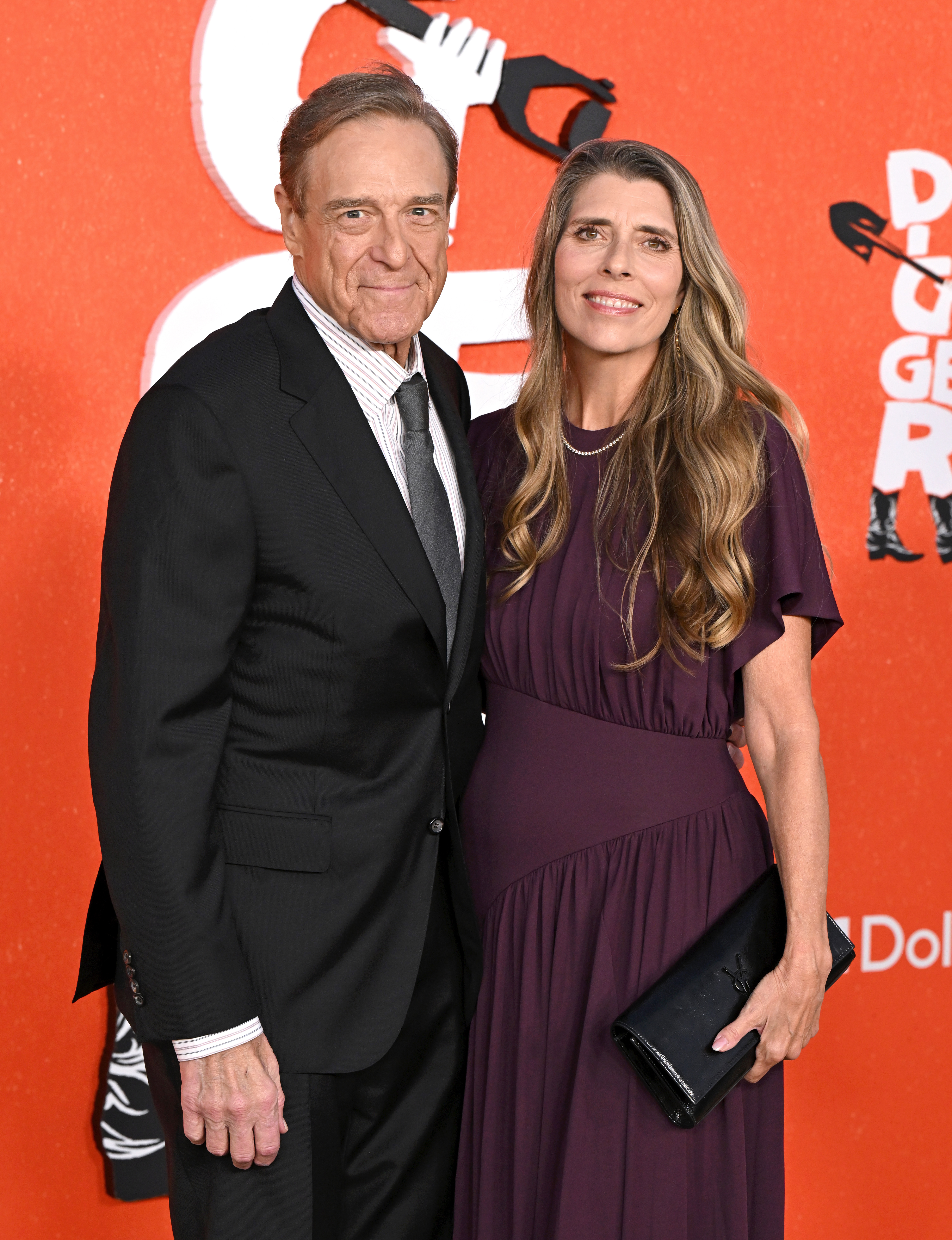 Goodman then posed with his wife, Anna Beth, who wore a plum-colored dress and carried a black clutch. Standing closely together, the couple marked another red carpet appearance decades after their earlier public outings.