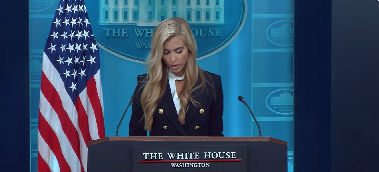 Katie Zacharia looks down at her notes while speaking at the White House briefing podium during her first press briefing on October 13. | Source: YouTube/The White House