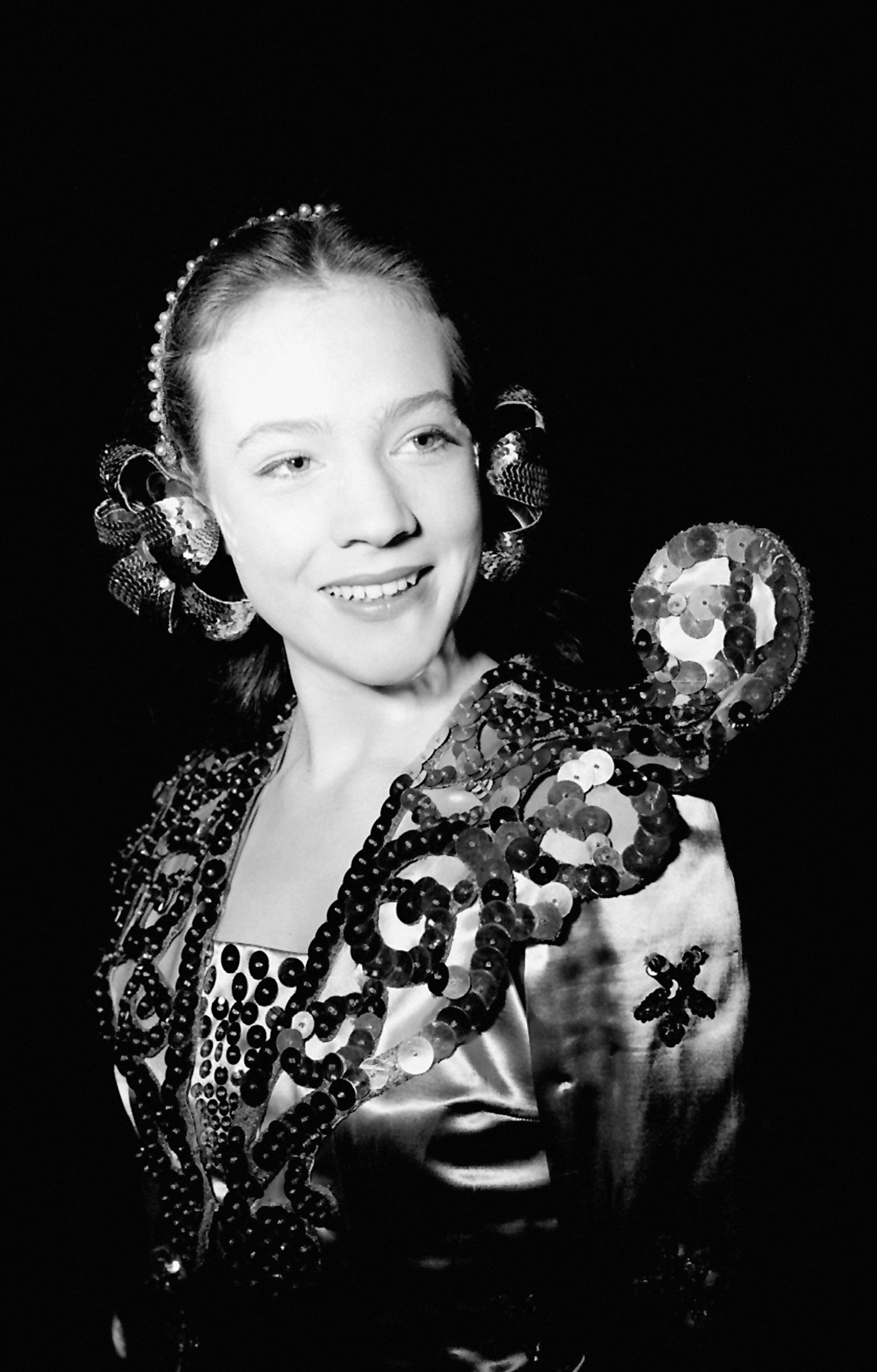 A 16-year-old Julie Andrews smiles during a dress rehearsal for Emile Littler's pantomime "Aladdin" at the London Casino, celebrated as the city's youngest Principal Girl. The rising British stage star wears an elaborate, shimmering theatrical costume embroidered with bold swirls of sequins and beads, paired with matching ornate hair ornaments framing her sleek updo.