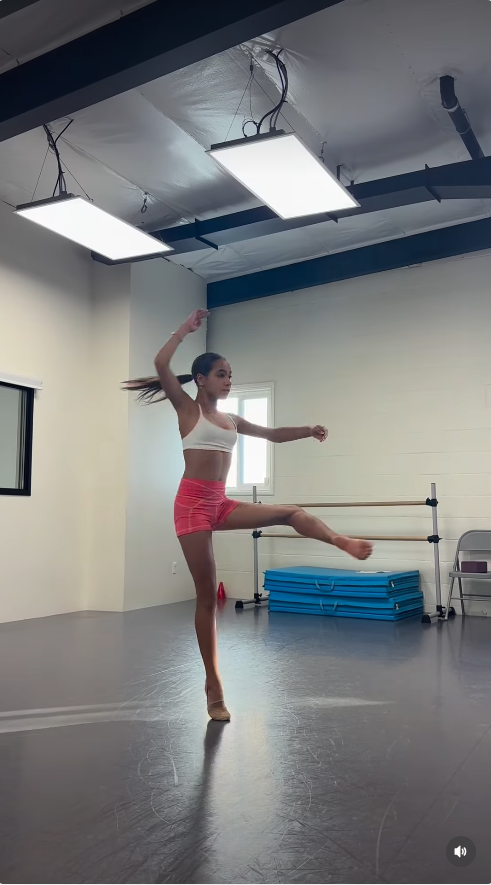 Fiona Lowe performs a dance routine in the studio, captured mid-movement with one leg extended and her arms positioned as she works through the choreography.