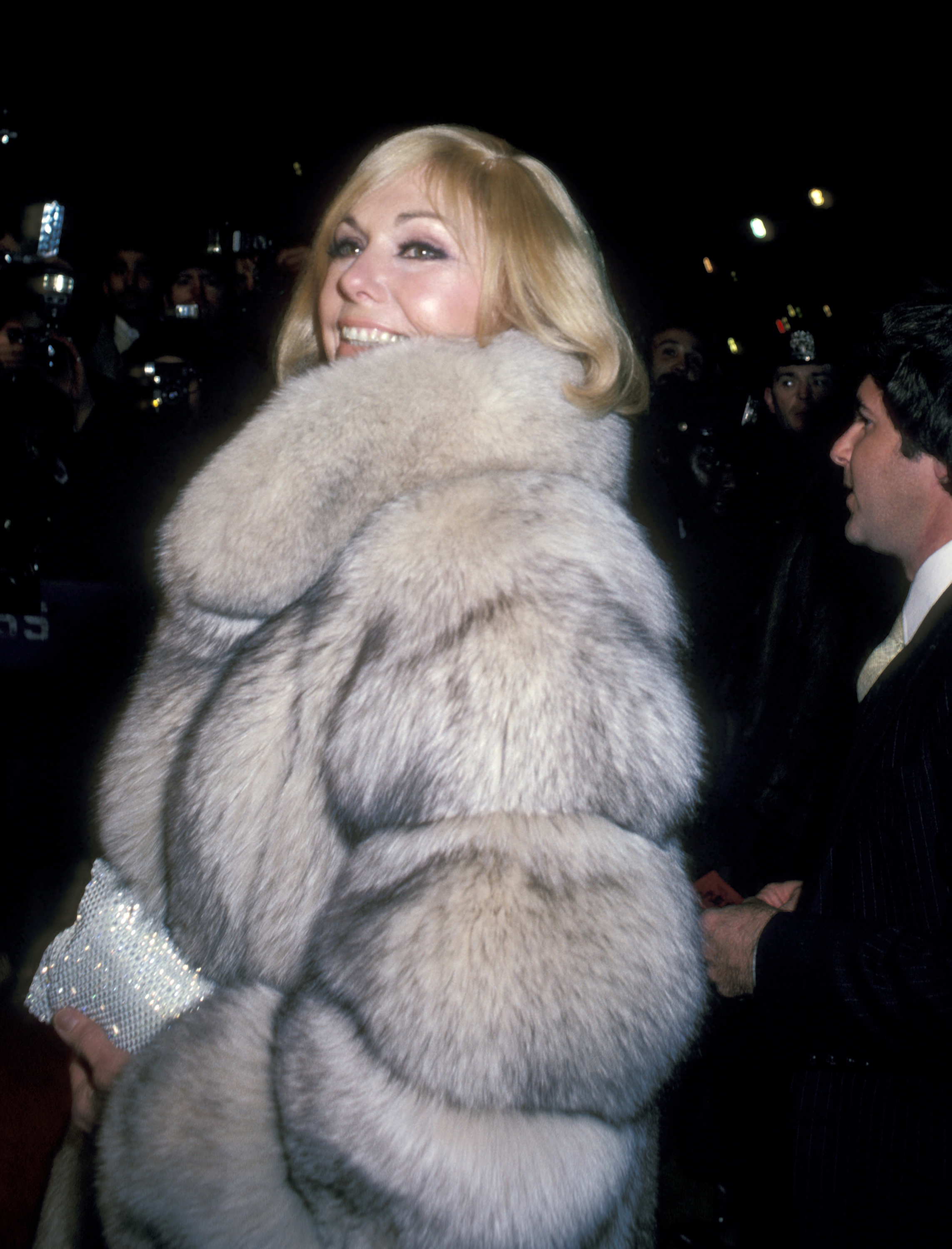 Kim Novak arrives at a movie-related event wearing a voluminous fur coat and carrying a sparkling clutch. | Source: Getty Images