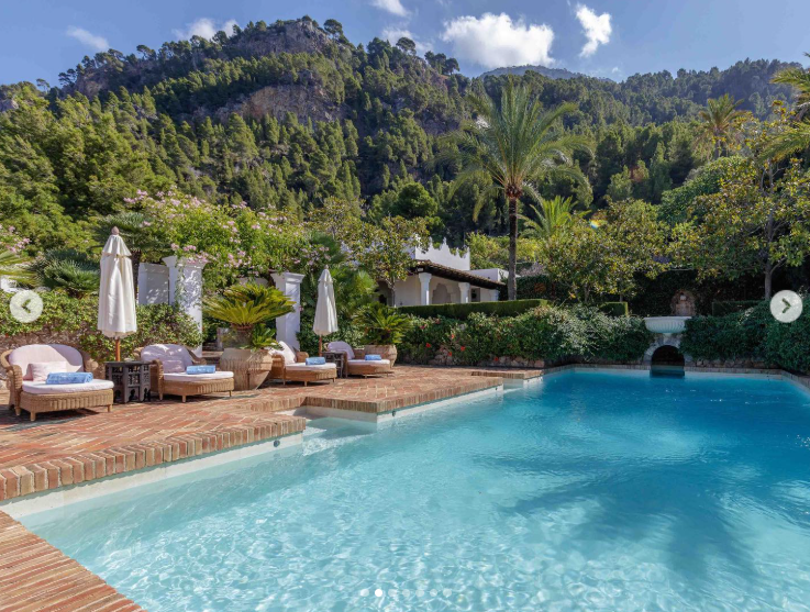 The outdoor pool is tucked into dense landscaping, with palms, flowering plants, and forested hills rising behind the water. Lounge chairs and shaded seating turn the area into one of the estate's more secluded places to unwind. | Source: Instagram/robbreport