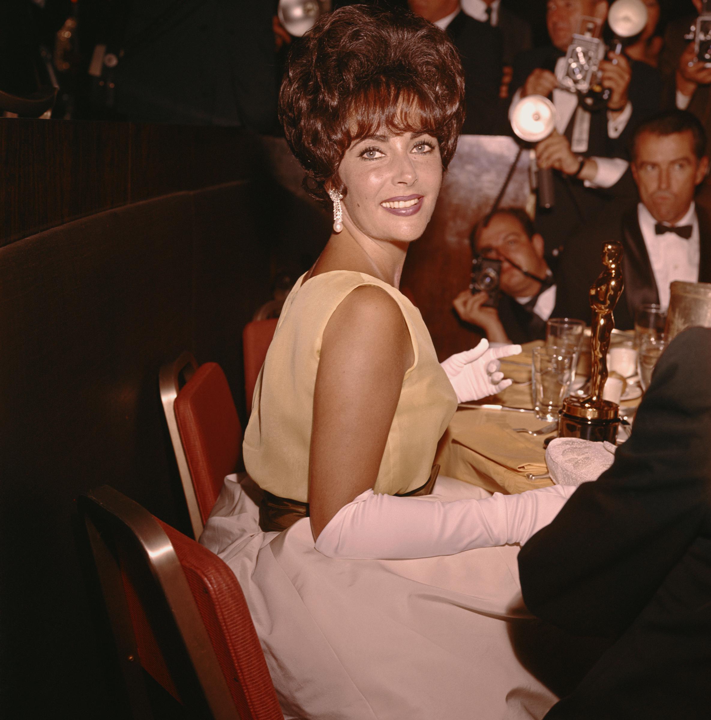 Elizabeth Taylor at the Academy Awards, seated at a table with her Oscar placed beside her, as photographers capture the moment | Source: Getty Images