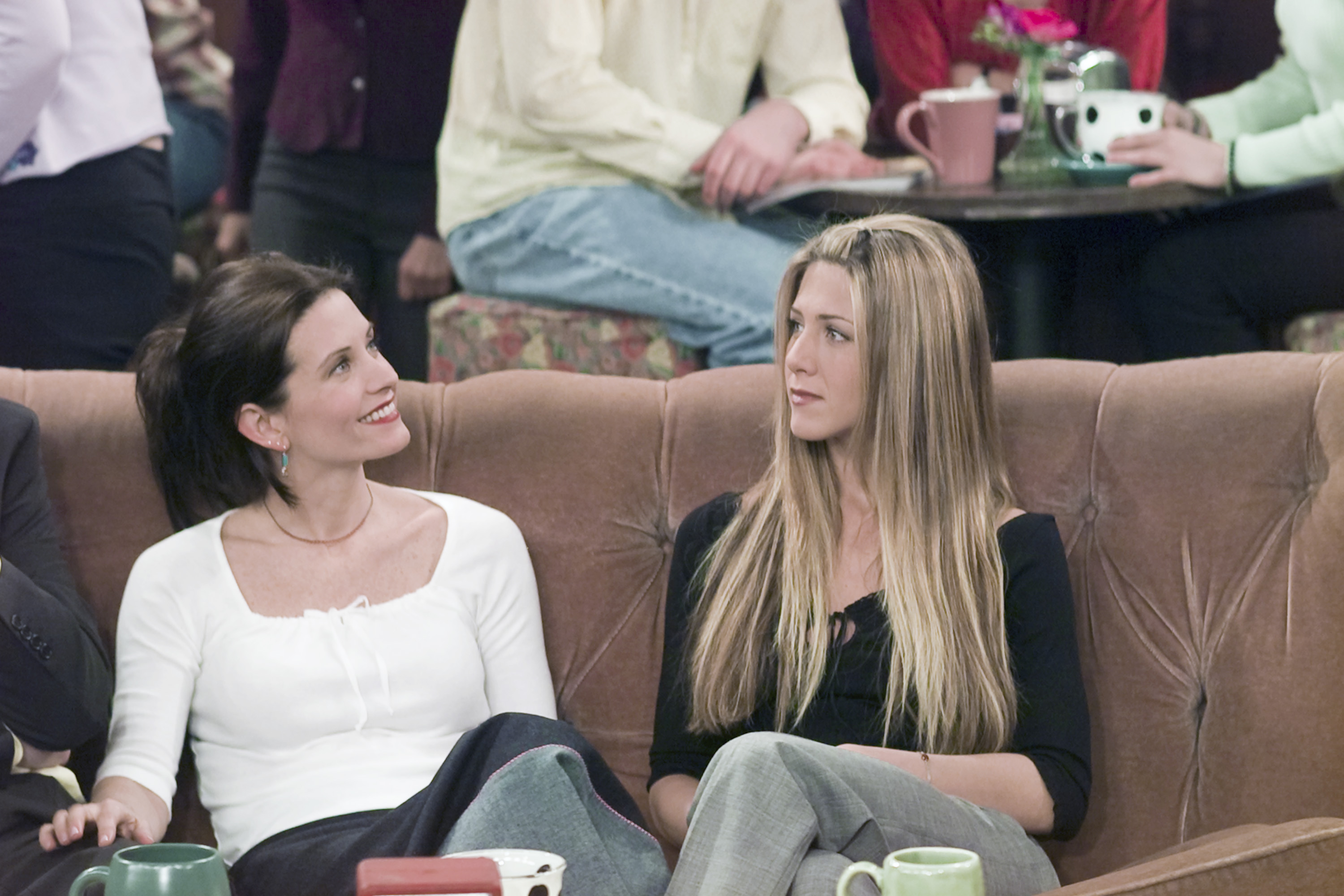 Courteney Cox as Monica Geller and Jennifer Aniston as Rachel Green seated in the iconic "Friends" café during the episode "The One Where Ross Meets Elizabeth's Dad." Even in character, their faces show a clear resemblance as they immerse themselves in the scene.