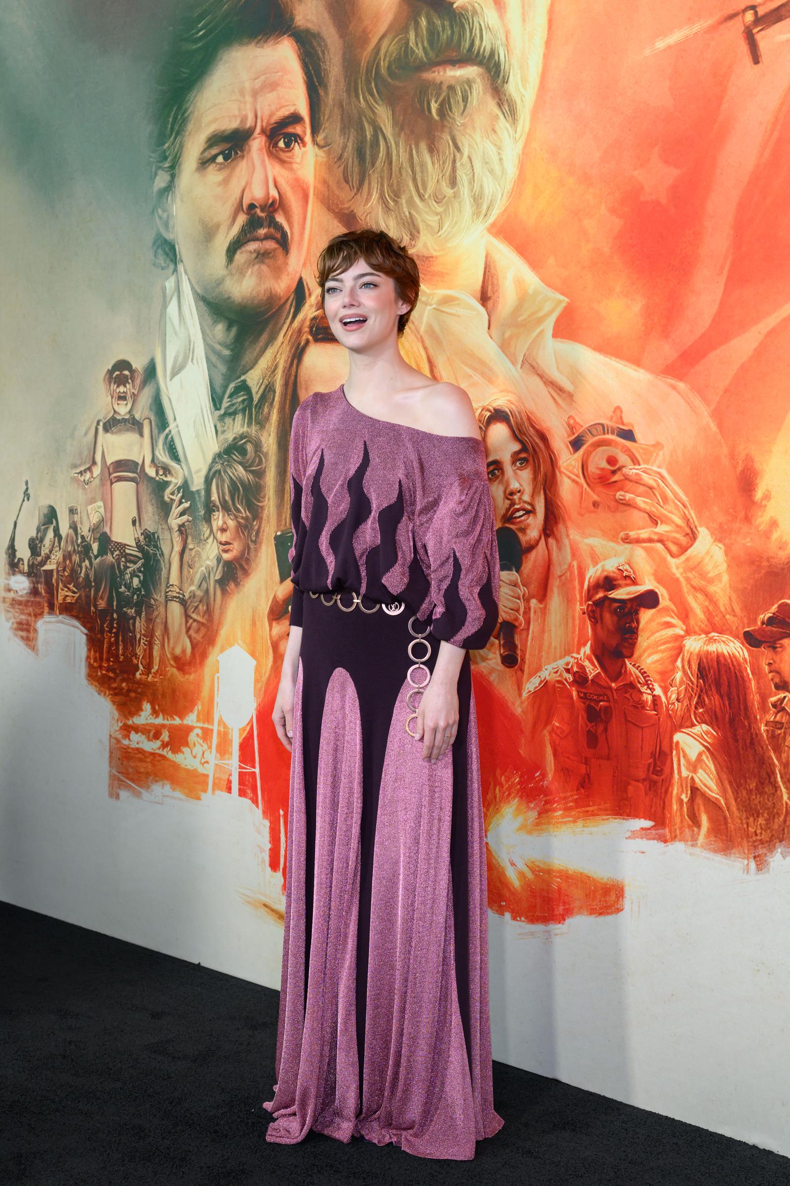 Stone stands with her mouth open, conveying a lively demeanor. In this full-length shot, the intricate design of her skirt can be appreciated. The background offers a broader view of the film's promotional artwork. For example, Austin Butler's likeness is clearly visible.