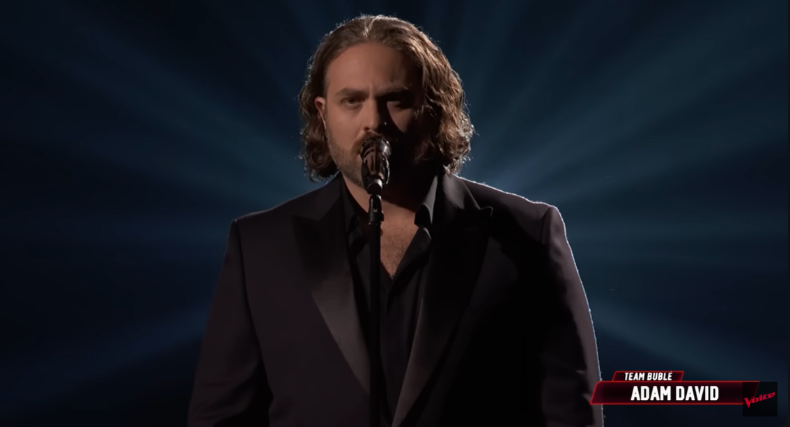 As the spotlight sharpens, Adam David begins to sing, revealing a focused expression as he delivers the opening lines | Source: YouTube/nbcthevoice