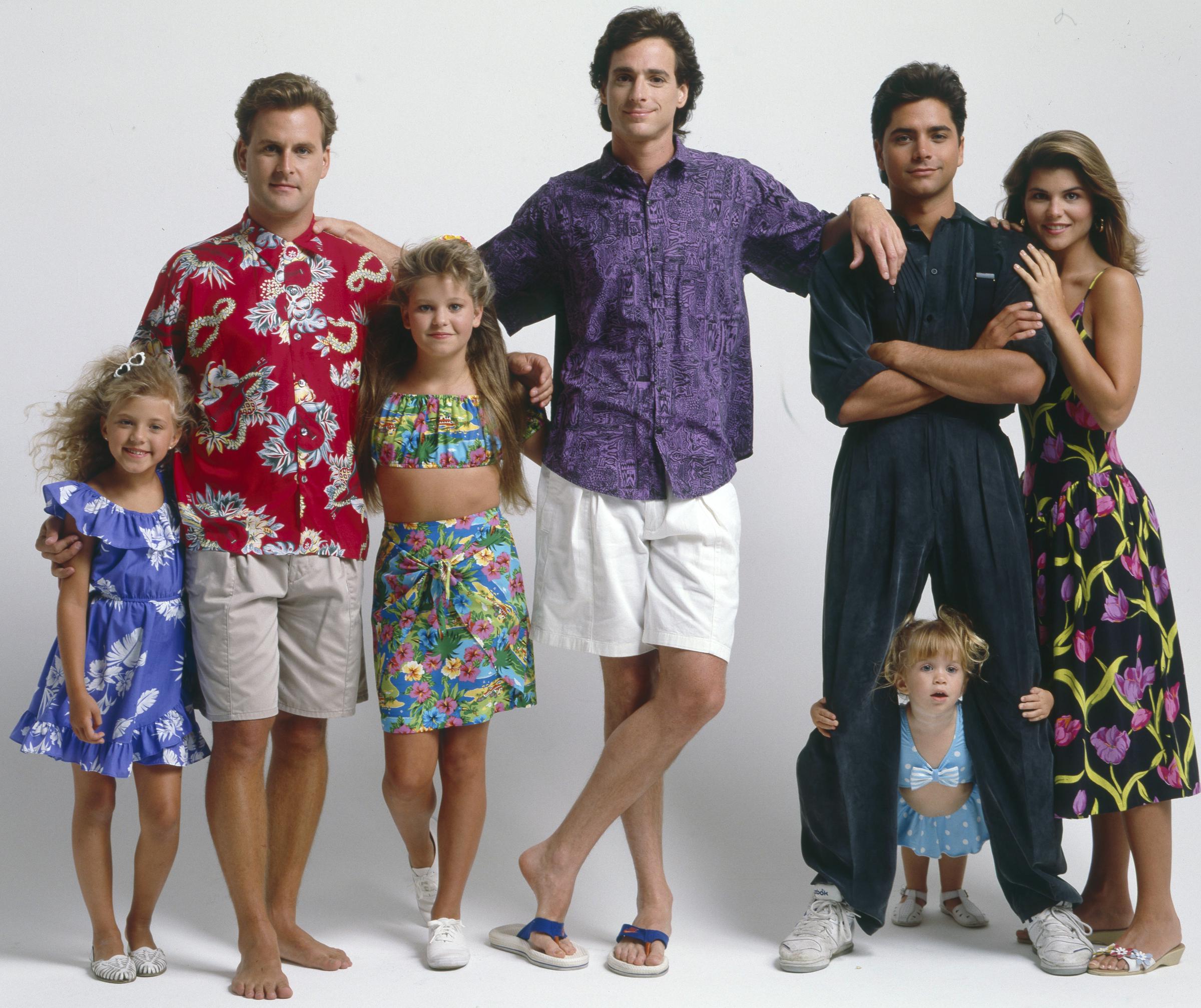 Jodie Sweetin, Candace Cameron Bure, John Stamos, and Lori Loughlin gather with castmates Bob Saget, Dave Coulier, and an Olsen twin for a Season 3 "Full House" shoot on August 8, 1989. Sweetin and Cameron Bure show off bright summer fashion, while Stamos poses effortlessly beside a radiant Loughlin. The portrait captures the early charm of a television family that fans would adore for decades.