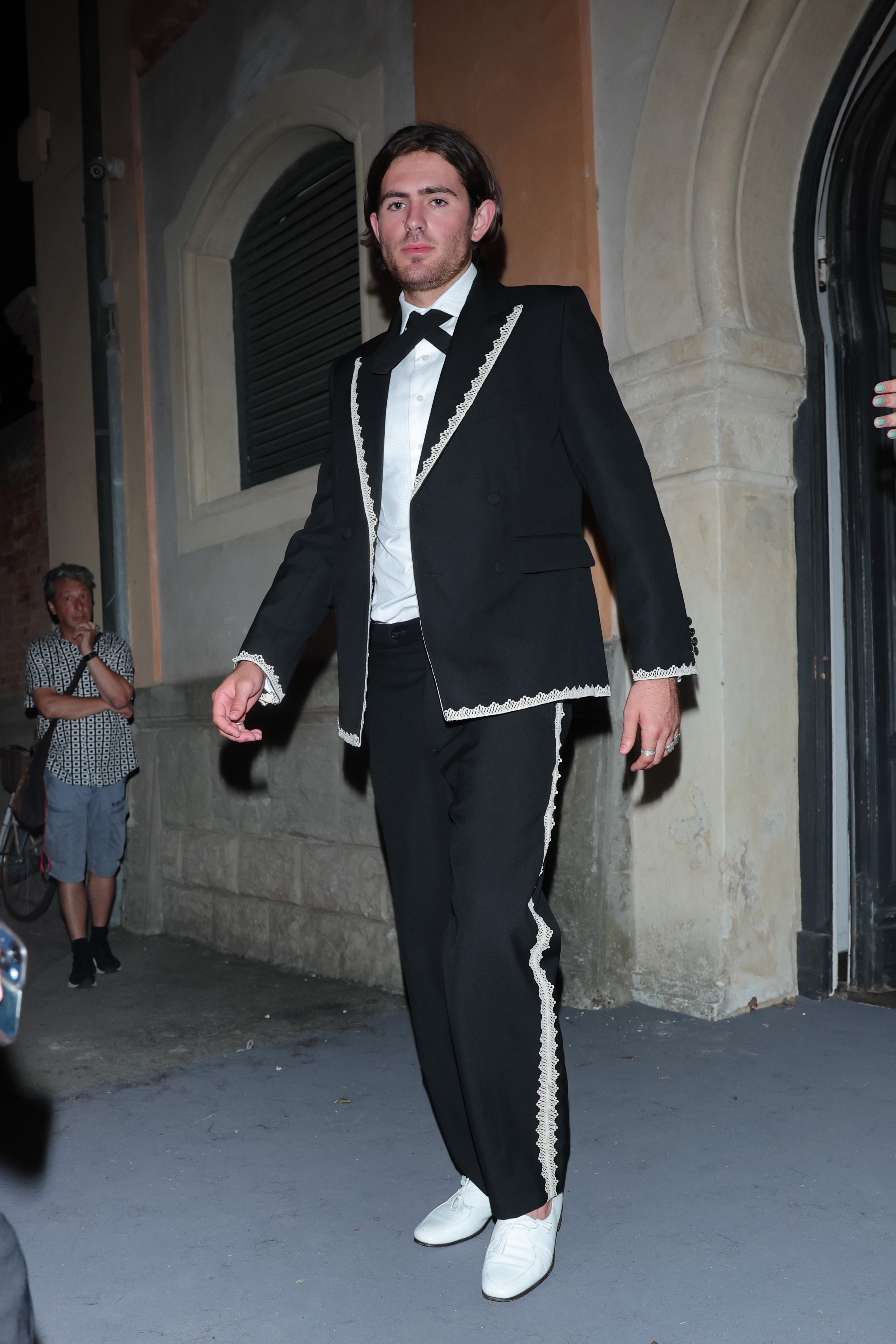 Indiana Affleck carried the ornate, Victorian-inspired motif down to his tailored black trousers, which featured the same intricate white scalloped lace trim running vertically along each side seam. Contrasting the dark suiting, a pair of crisp, ivory-white pointed dress shoes anchored the look with an eye-catching, dapper finish during the 83rd Venice International Film Festival on September 8, 2026. | Source: Getty Images
