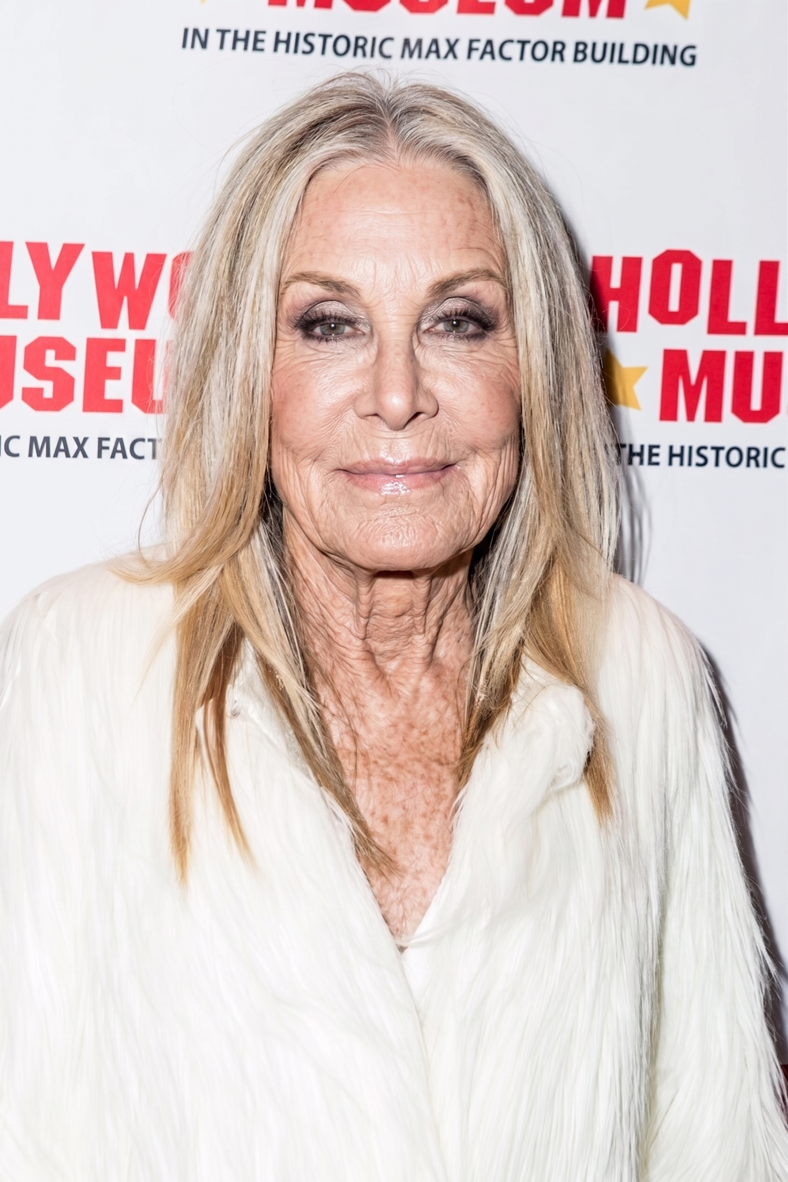 AI reimagines Joan Van Ark arriving at a Hollywood event in an elegant white coat, envisioning the actress with naturally aged features that complement her signature sophistication while preserving the warmth and confidence seen throughout her career. | Source: Gemini