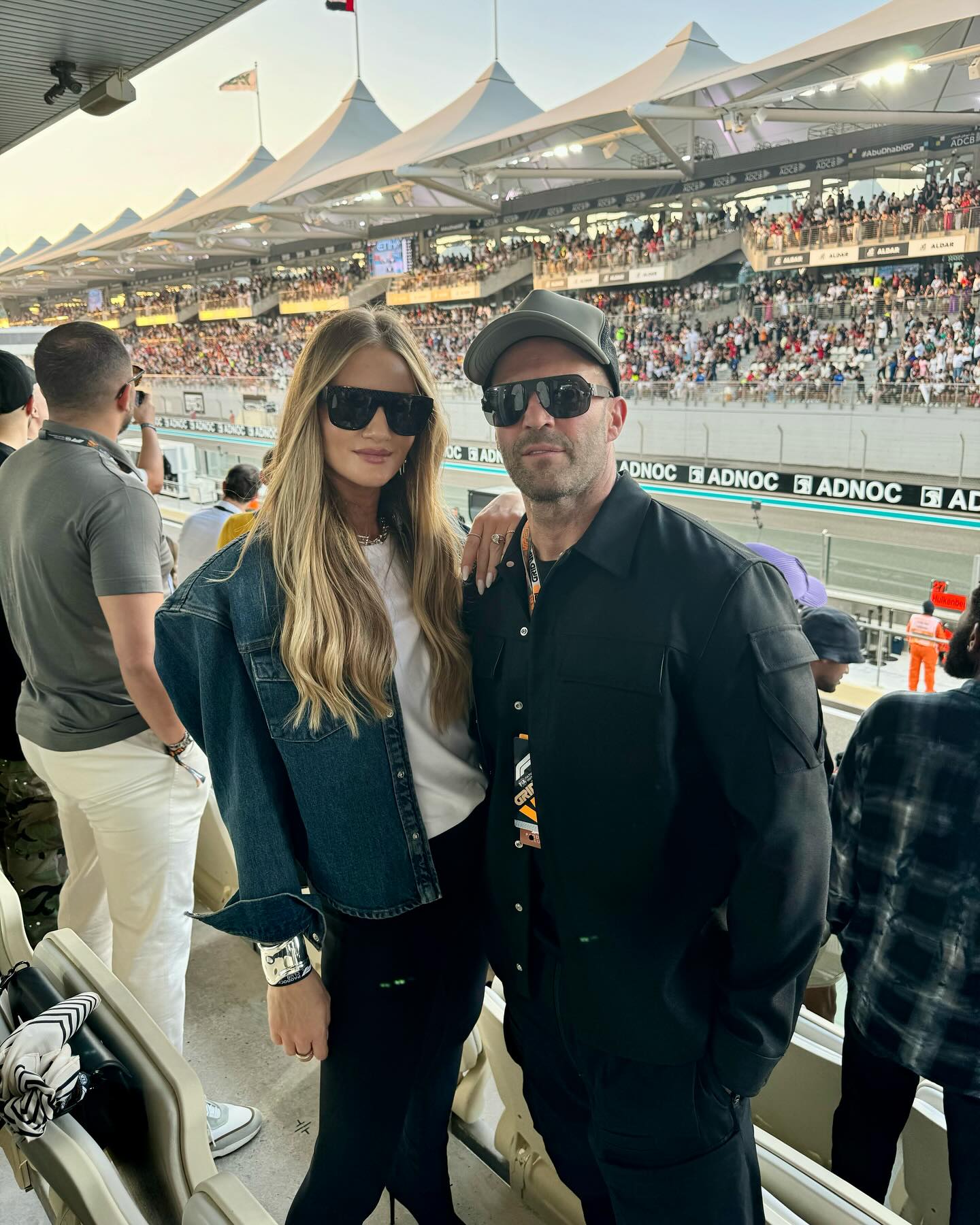Rosie Huntington-Whiteley and Jason Statham pose trackside at a packed racing event, both sporting dark sunglasses and effortlessly cool looks. | Source: Instagram/rosiehw