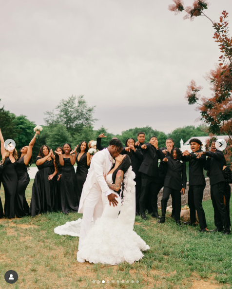 Travis Hunter and Leanna Lenee kiss in front of their bridesmaids and groomsmen, dated May 2025 | Source: Instagram/db3_tip