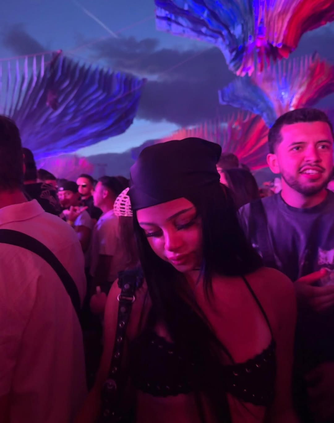 Harlow Winter Kate Madden looks downward while posing in a dark festival outfit under purple and pink lights at Coachella 2026. The nighttime crowd and glowing backdrop frame Kate in a moody concert moment. | Source: Instagram/katemaddennn