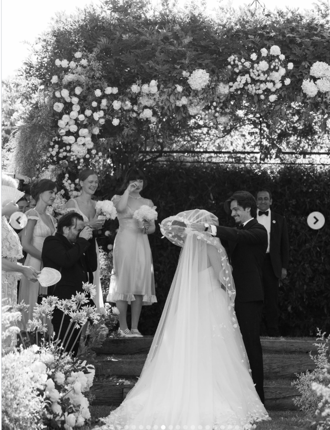 On July 3, 2026, beneath the flower-covered arch, Dylan Lee gently lifted his bride's veil during the intimate garden ceremony as their smiling wedding party looked on. | Source: Instagram/thierryjoubertphotography