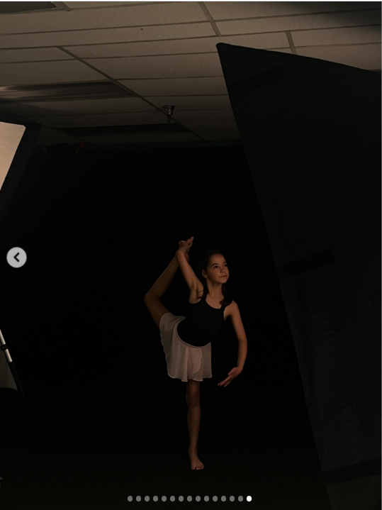 Fiona appears in a striking dance portrait, dressed in a black sleeveless outfit with a pale pink skirt as she balances on one leg and raises the other high beside her. Set against a dark studio backdrop, she holds the pose with a calm, focused expression, placing her love of dance at the center of the final image.