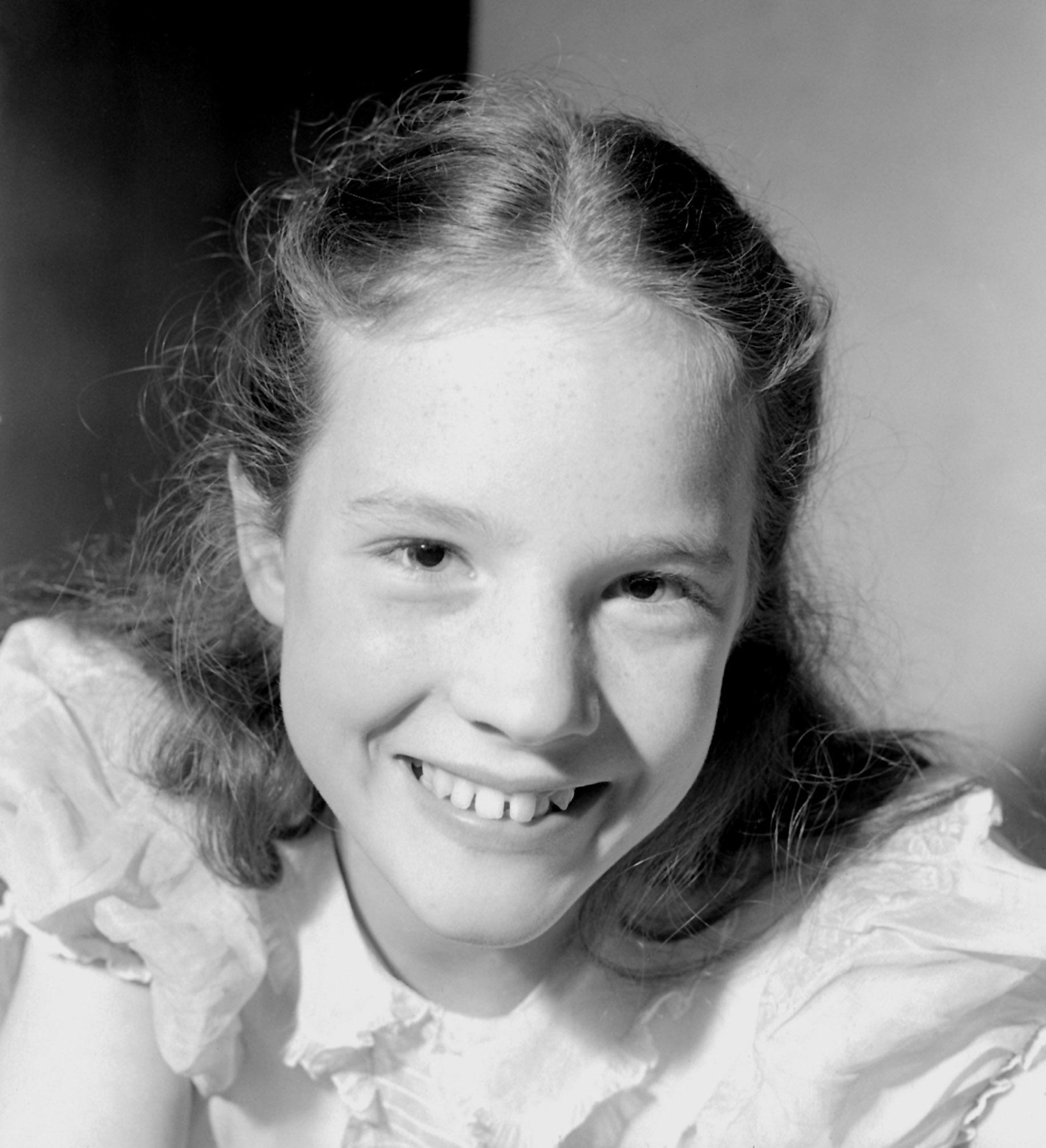 A radiant 13-year-old Julie Andrews smiles warmly in a vintage close-up portrait taken on October 14, 1948, celebrating her selection as the youngest solo performer chosen for the Royal Command Variety Performance at the London Palladium. The young coloratura soprano wears a ruffled white dress with her hair swept back away from her face, showing off her natural freckles and joyful toothy grin.