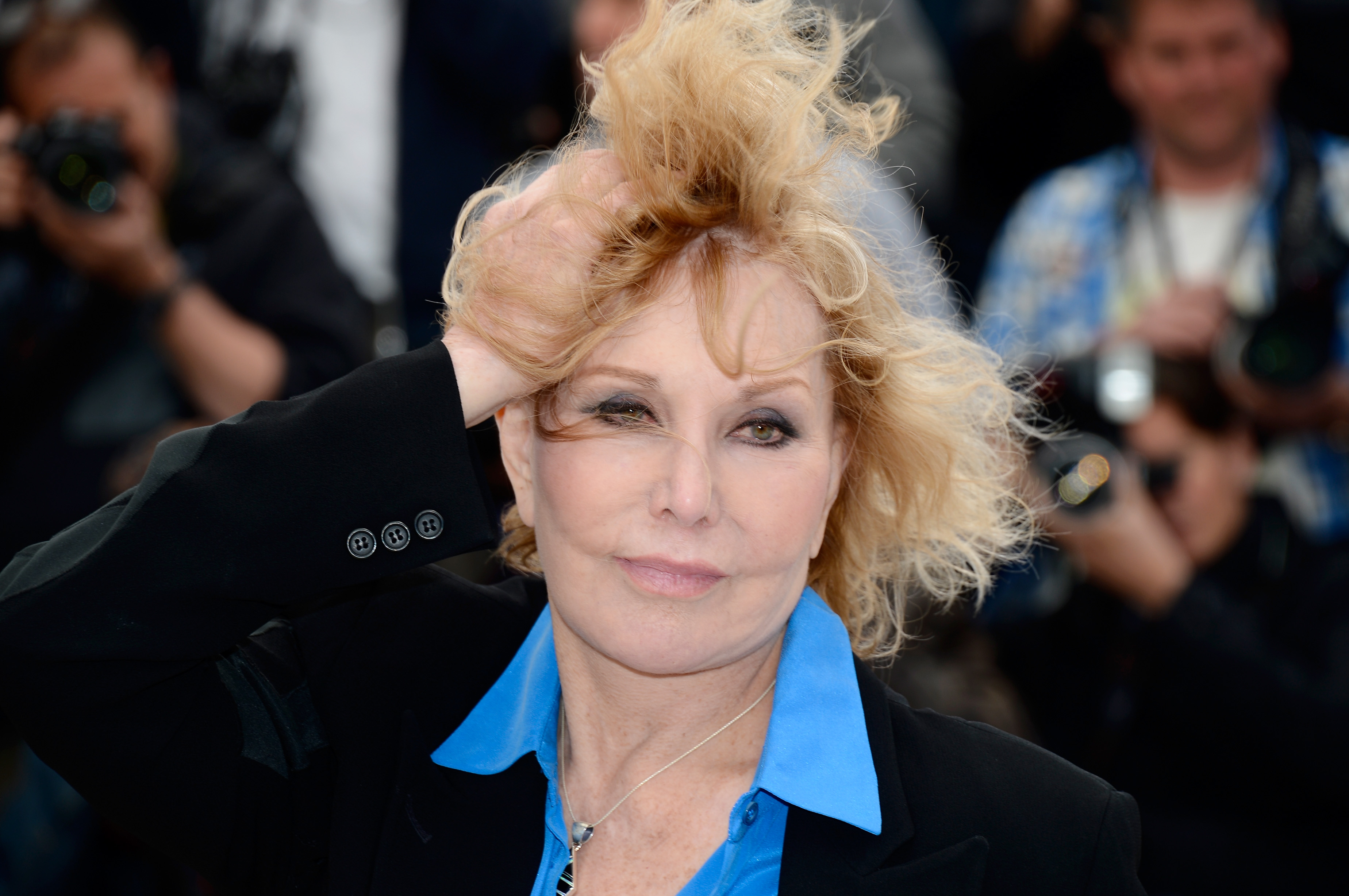 Kim Novak adjusts her hair while posing for photographers at the Cannes Film Festival in May 2013, wearing a black blazer and bright blue shirt. | Source: Getty Images