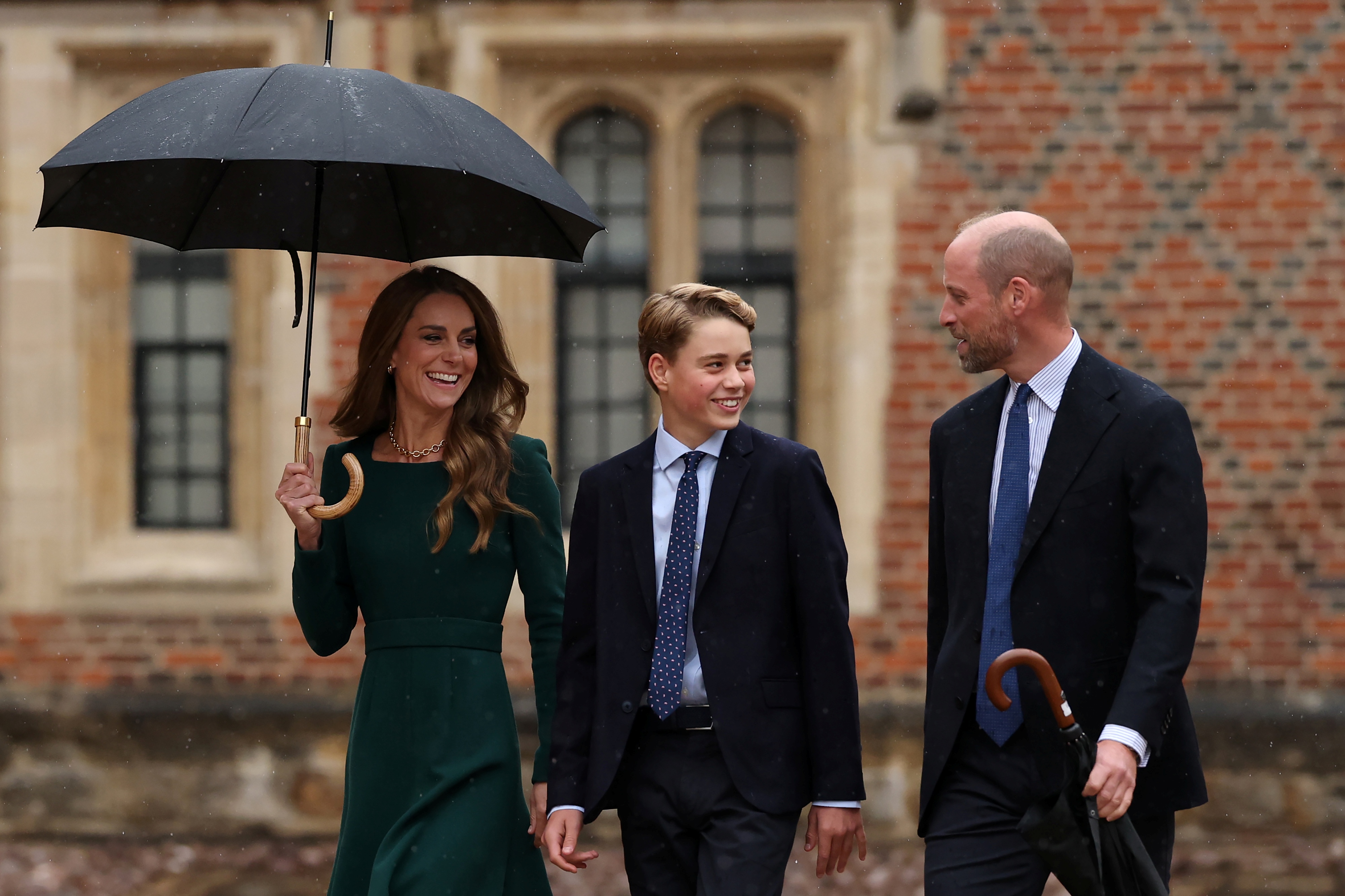 George turned toward William during a lighthearted moment as Catherine walked beside them under an umbrella. The family arrival captured the parents accompanying their eldest son into his next stage of education.