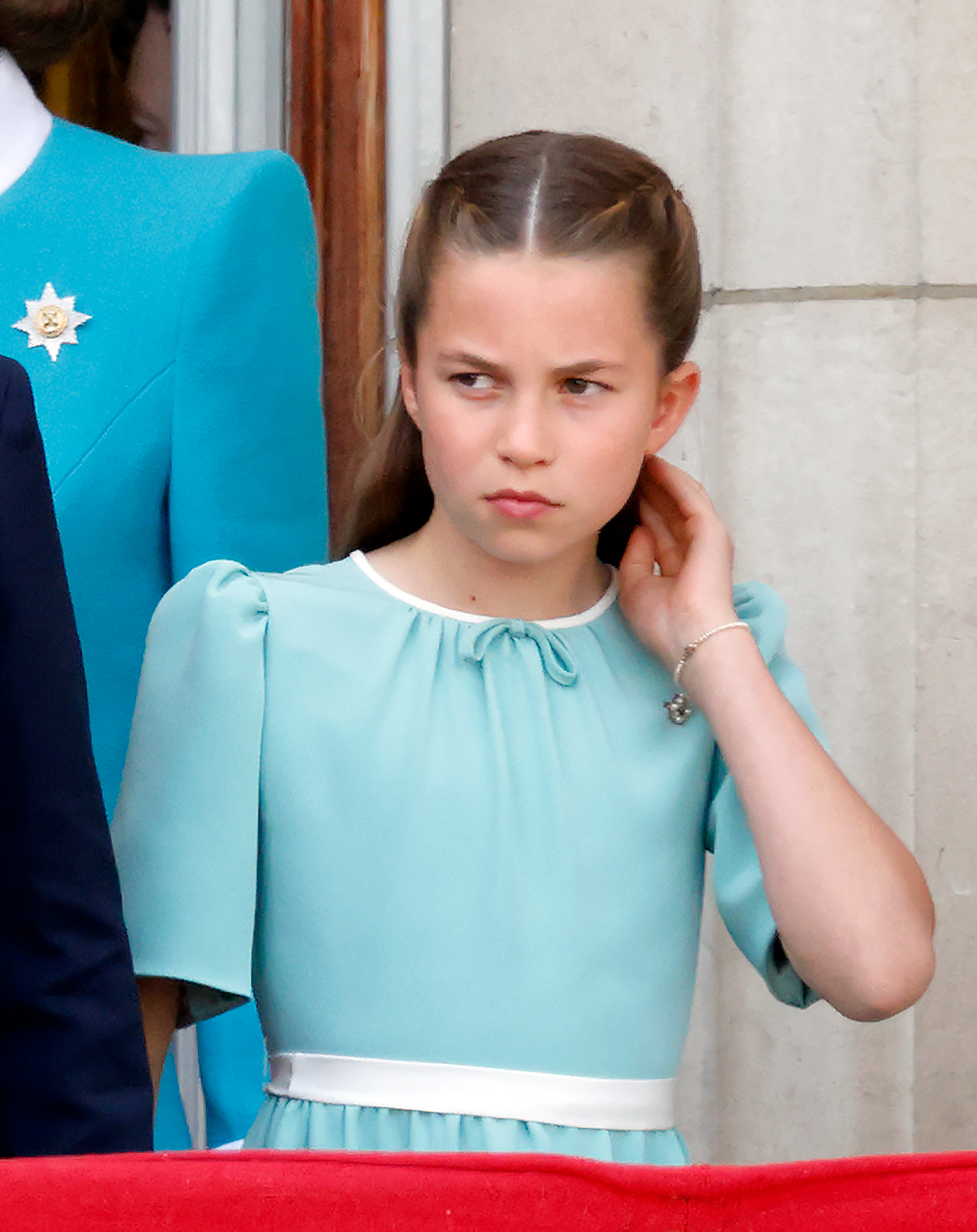 Princess Charlotte of Wales, in her beautiful white and aquamarine dress, gorgeous hairdo, and bangle, touches her hair and watches an RAF flypast from the balcony of Buckingham Palace during the 2025 Trooping The Colour in London, England on June 14, 2025.