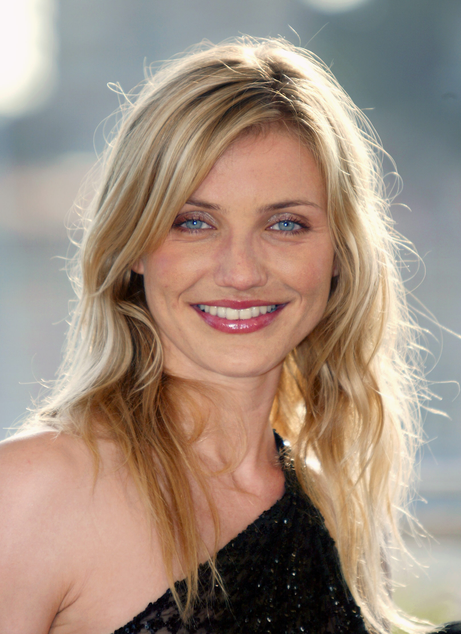 Cameron Diaz poses for photographers during a photocall for "Gangs of New York," wearing a black, one-shoulder textured dress, with her long blonde hair styled in soft waves and a radiant smile highlighted by natural, glowing makeup.