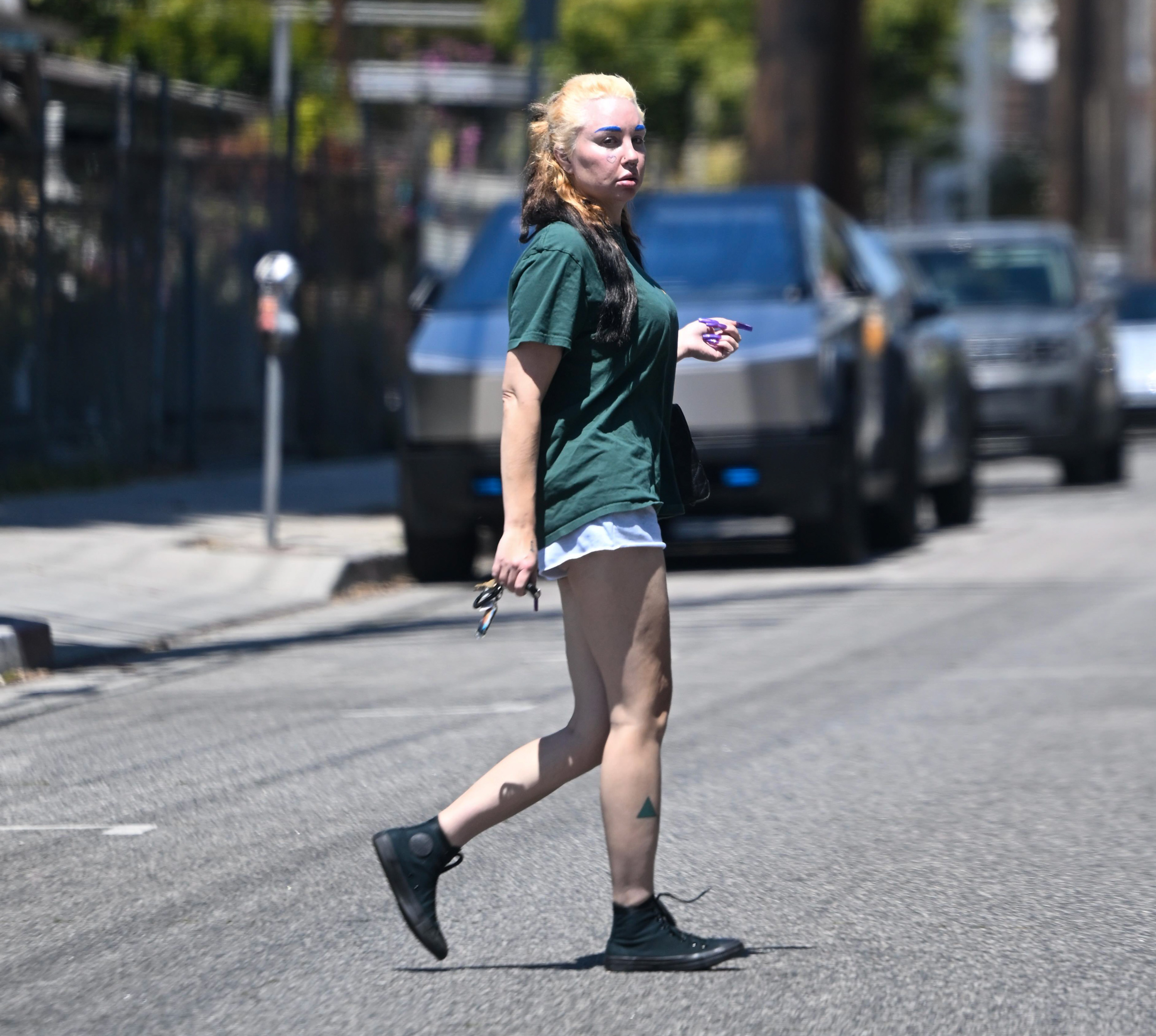 Amanda Bynes was photographed crossing a street in Los Angeles wearing an oversized green T-shirt, white shorts, and black high-top sneakers. She carried her keys and a small purple item while her two-toned hair, blue eyebrows, facial piercings, and leg tattoos were on display.