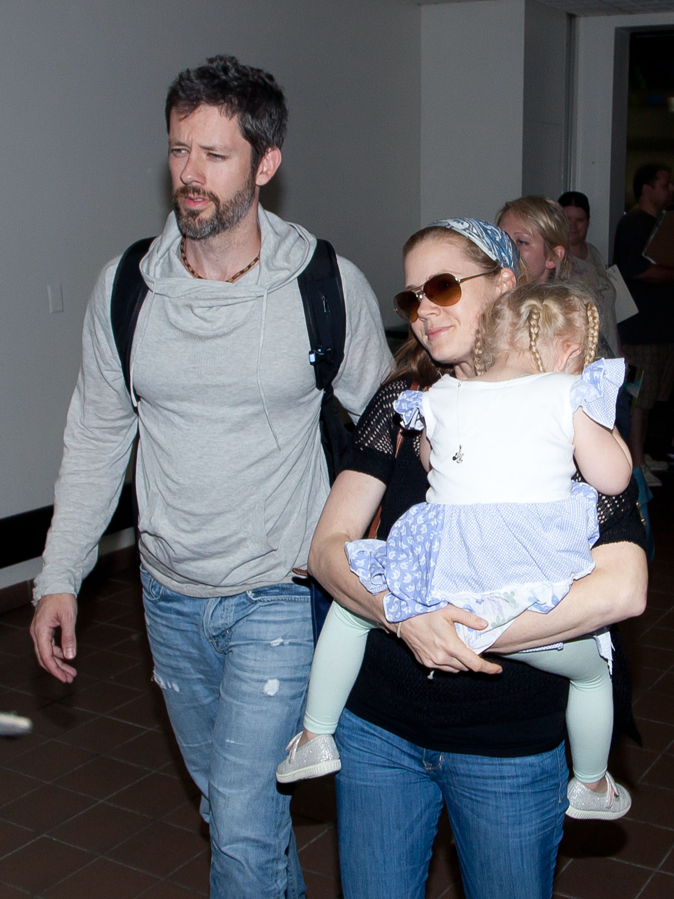 Amy Adams and Darren Le Gallo walk through Los Angeles International Airport with their young daughter, Aviana Olea Le Gallo, who rests in Amy's arms. The family appears relaxed while making their way through the terminal together.