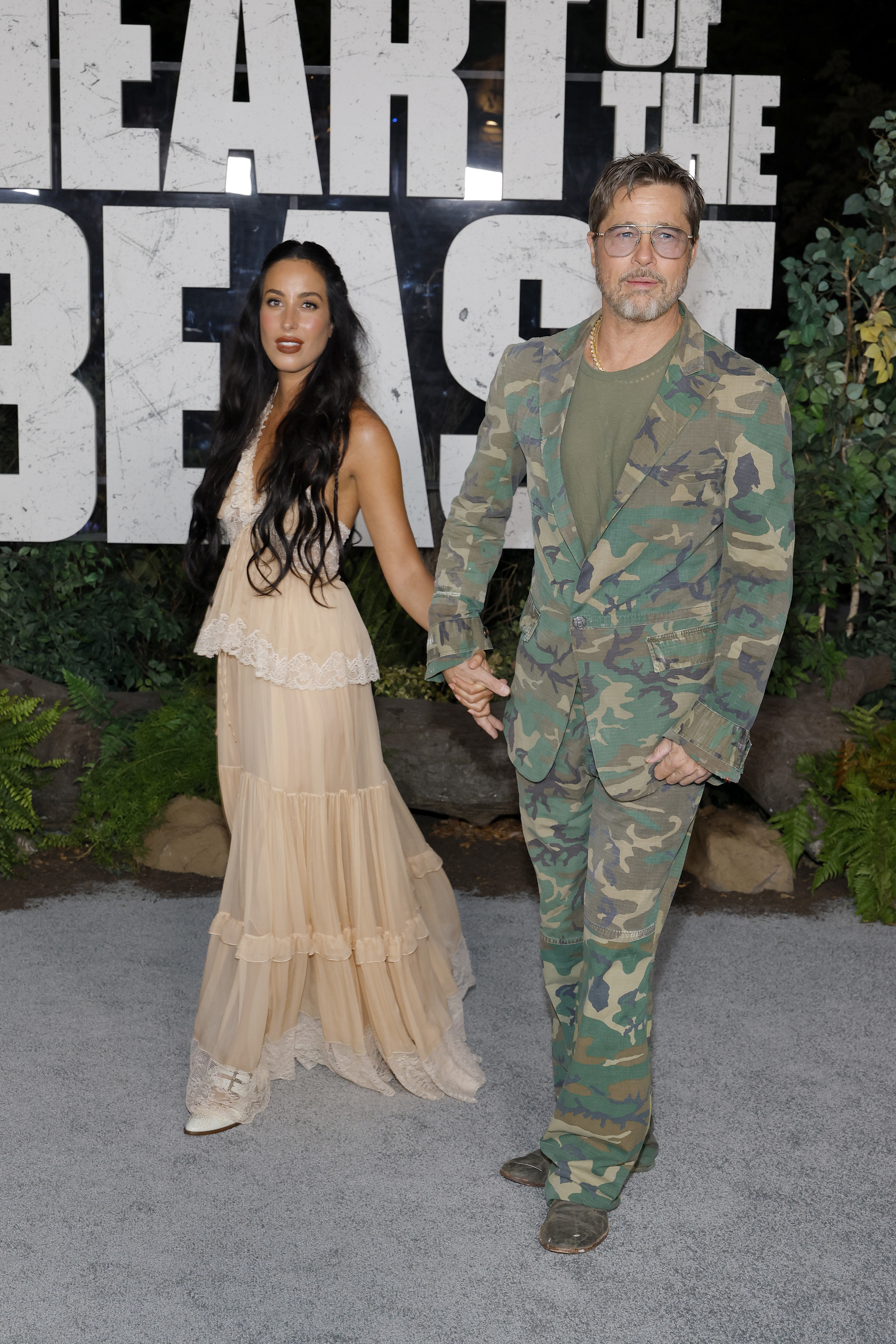Ines de Ramon and Brad Pitt walked hand-in-hand along the carpet at Paramount Pictures' "Heart Of The Beast" global premiere held at FirstBank Amphitheater on September 16, 2026, in Franklin, Tennessee. Pitt embraced a bold utilitarian aesthetic in a camouflage-print suit jacket and matching flared trousers layered over an olive green crewneck shirt and accessorized with tinted wire-frame glasses, while de Ramon complemented him in a bohemian-style, tiered champagne lace maxi dress with soft waves cascading down her shoulders. | Source: Getty Images