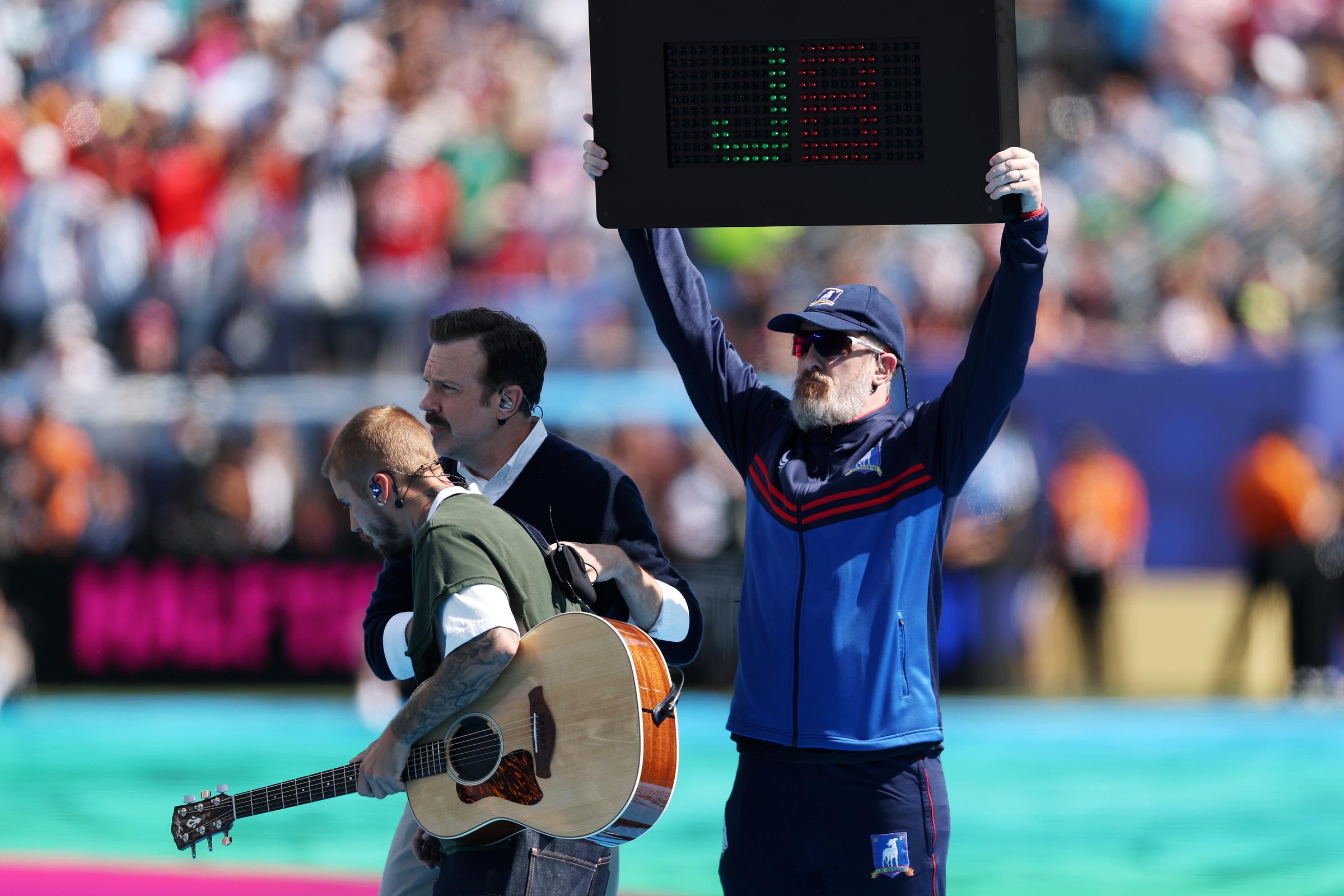 A stadium crew member holds an electronic board displaying a giant "J" and "US" during Justin Bieber's halftime appearance, adding a branded visual to the musician's low-energy acoustic interlude. | Source: Getty Images
