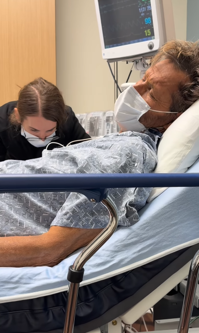 A masked Duguay lies in a hospital bed while a woman bends over beside him. The image offers a personal glimpse of the medical challenges his family documented as they continued hoping for his recovery. | Source: Instagram/mrs__shay