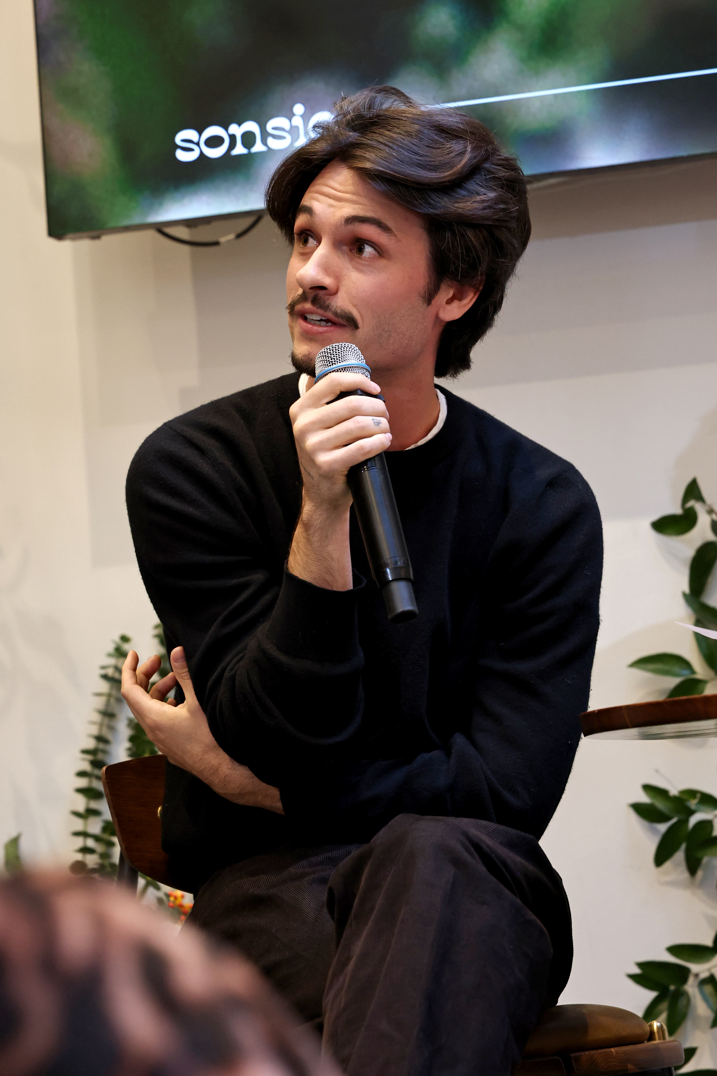 Dylan speaks during the "Sonsie Garden" event with Shopify on October 24, 2025, in New York City. He wears a black sweater and holds a microphone while seated beneath a screen bearing the brand's name.