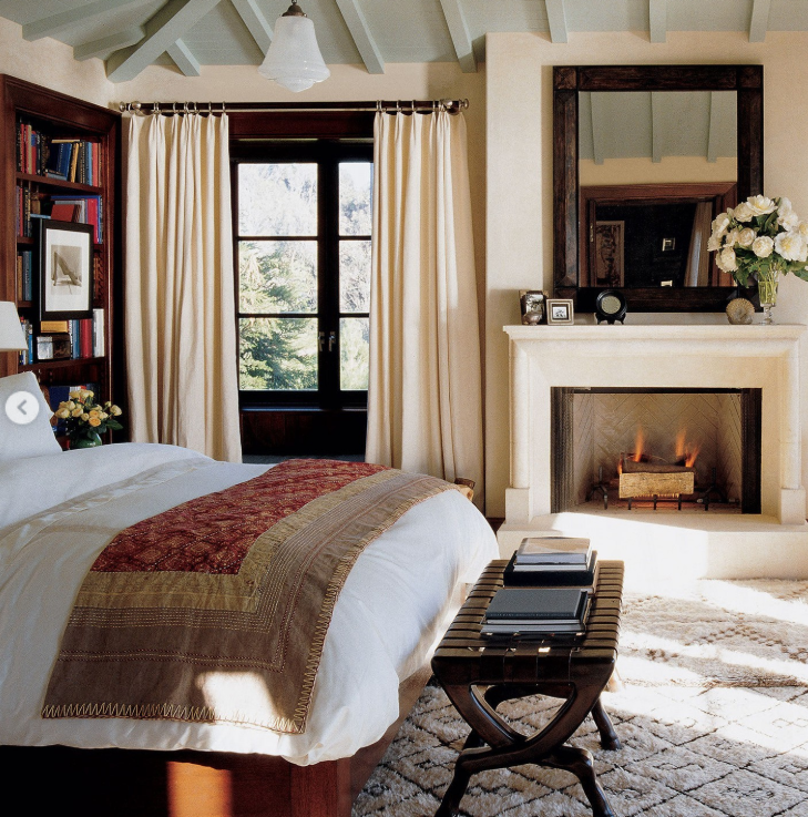 A bedroom combines dark wood, pale walls and exposed ceiling beams with a fireplace and patterned textiles. The mix reflects the balance Cindy and Rande sought between her preference for warmth and his more modern style. | Source: Instagram/elledecor