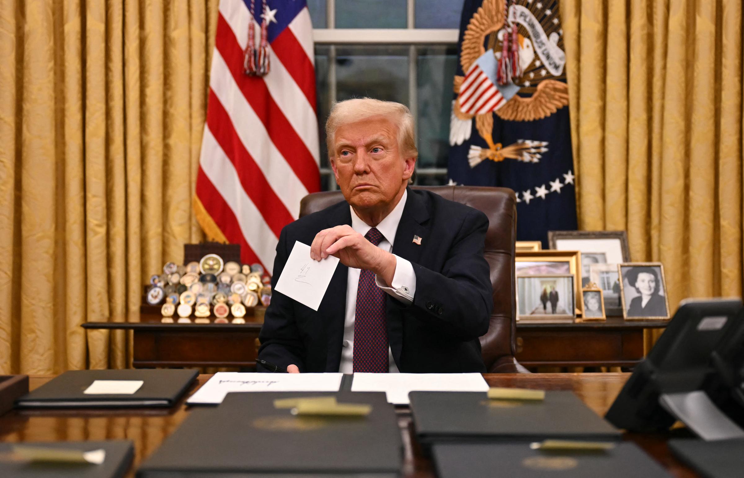 Donald Trump holds up outgoing Joe Biden's letter as he signs executive orders in the Oval Office of the White House in Washington, D.C., on January 20, 2025 | Source: Getty Images