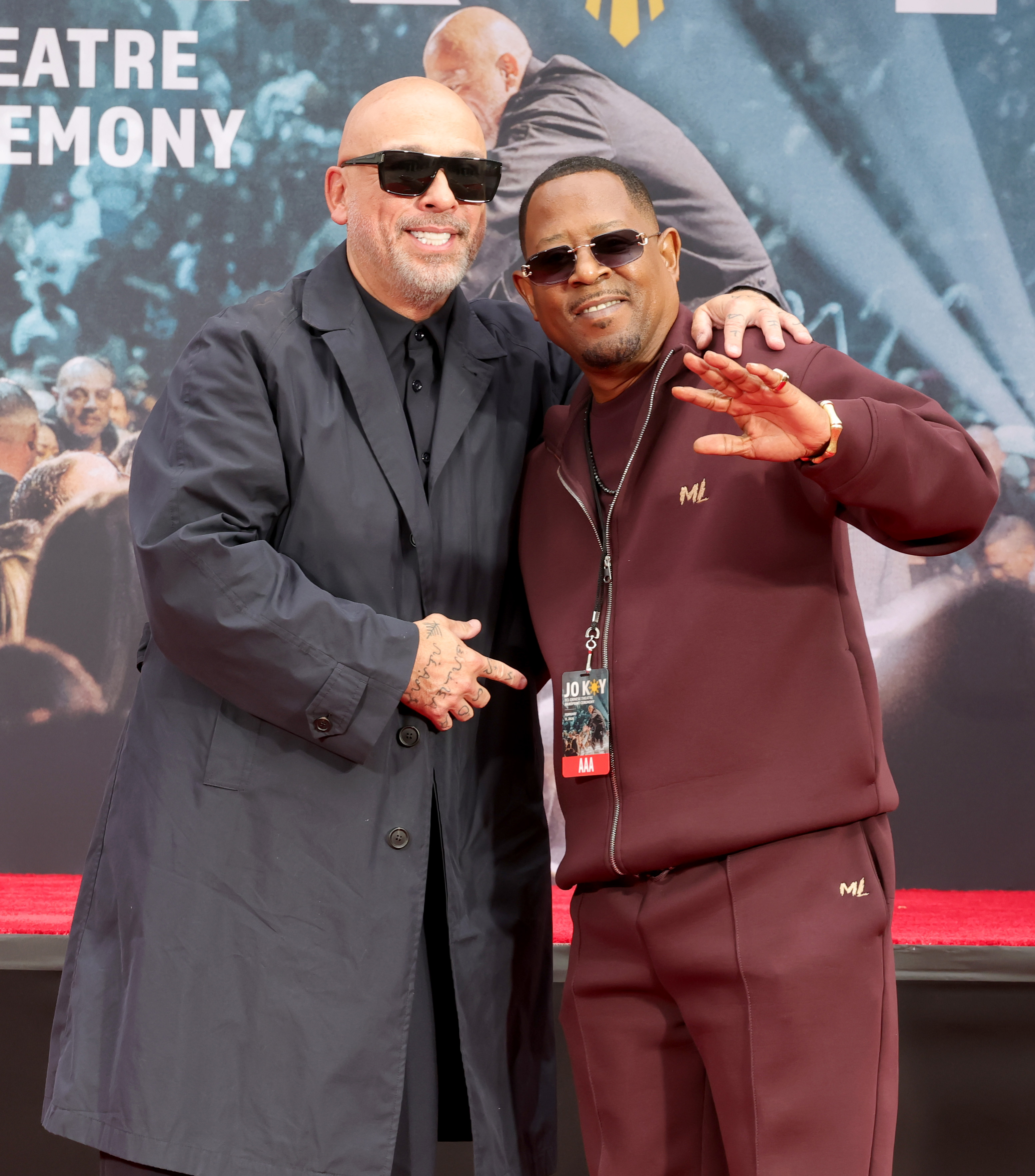 Jo Koy and Martin Lawrence pose together at the TCL Chinese Theater during Jo Koy’s hand and footprint ceremony in Hollywood. Jo Koy, in a long black coat and sunglasses, smiles as he points toward Martin. Martin, in a burgundy tracksuit with “ML” detailing and tinted sunglasses, raises his hand in a relaxed wave.
