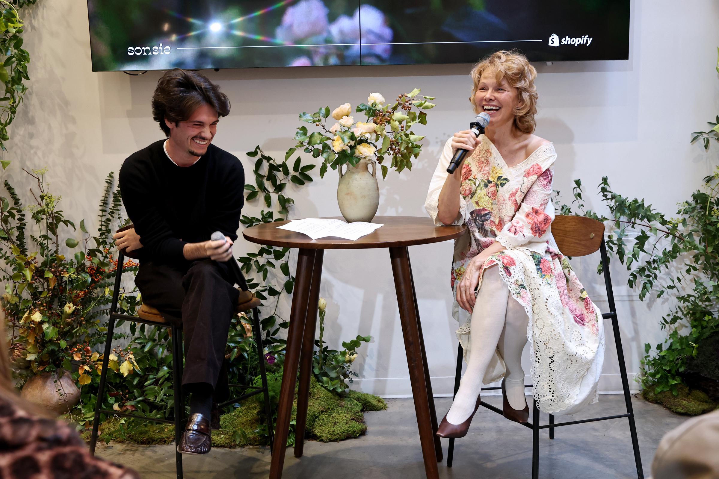 Pamela and Dylan speak to a full audience during the "Sonsie Garden" panel event in New York. Seated in front of a floral arrangement, they address guests from the stage.