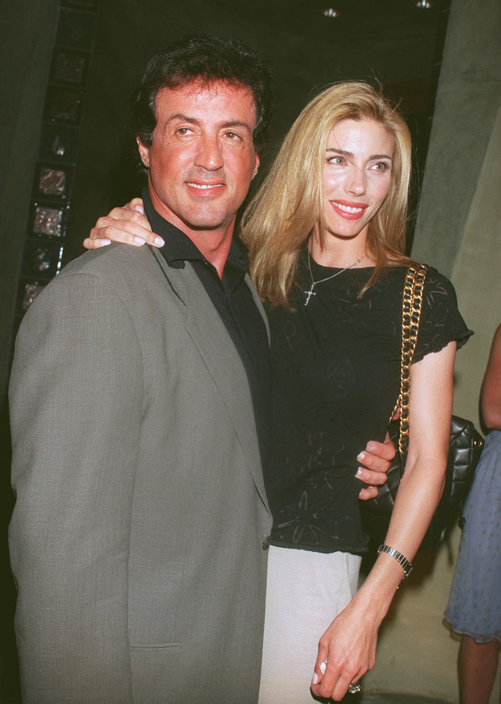 Sylvester Stallone and his wife, Jennifer Flavin, were photographed outside Spago restaurant in Beverly Hills, California, on July 8, 1999. Flavin rested one hand on her husband's shoulder as the actor held her at the waist, with both turning toward nearby cameras. The outing came two years after their London wedding, by which point the couple had moved beyond the earlier breakups that marked their courtship years before.