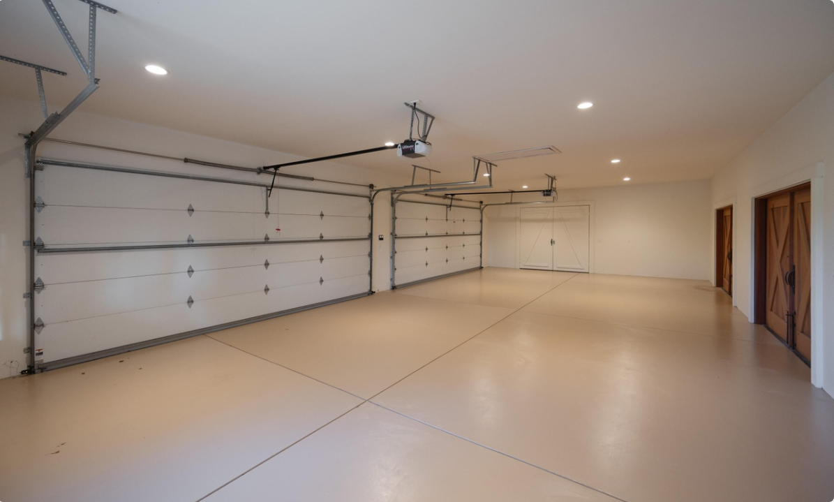 The property features a spacious garage with multiple vehicle bays, a smooth floor, overhead garage-door systems, and wooden storage-room doors. | Source: Redfin