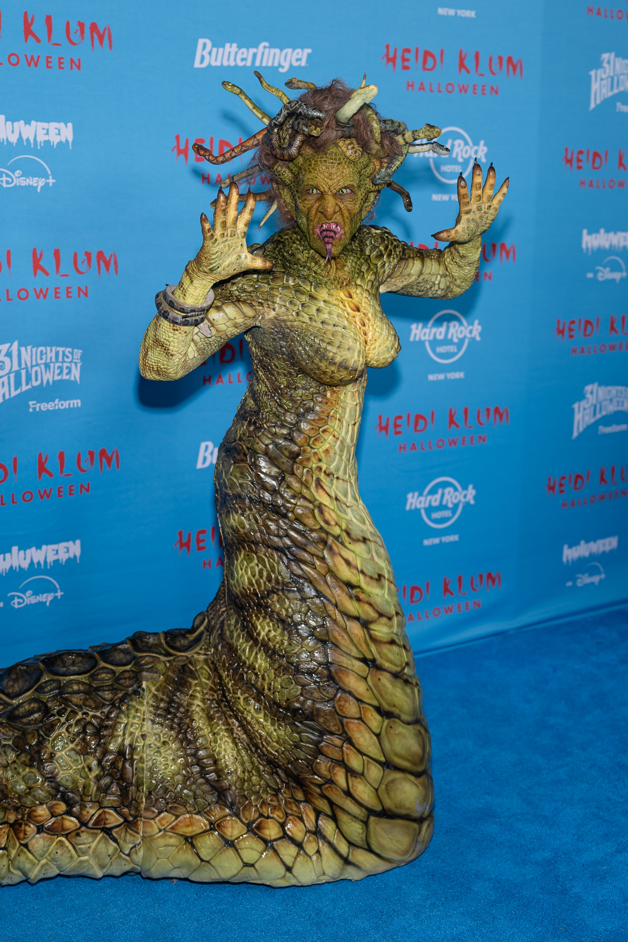 At her 24th Annual Halloween Party in New York, Klum stunned in a full-body Medusa costume that blurred the line between fashion and creature design. Covered in hyper-detailed reptilian scales, she slithered onto the blue carpet with a lifelike snake tail and a headpiece of snarling serpents. Yellow reptile contacts and fanged prosthetics completed the terrifying, myth-inspired look — another over-the-top transformation from the undisputed queen of Halloween.