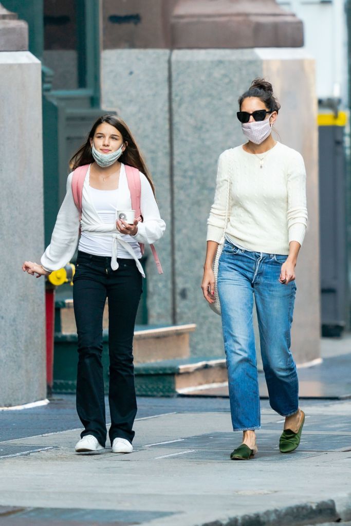 In this pandemic-era moment, a grown Suri Cruise is seen walking alongside her mother, Katie Holmes, both wearing face masks as they navigate the city streets. Their coordinated steps and covered expressions reflect the realities of a changed world, where even the most familiar faces blend into the crowd.