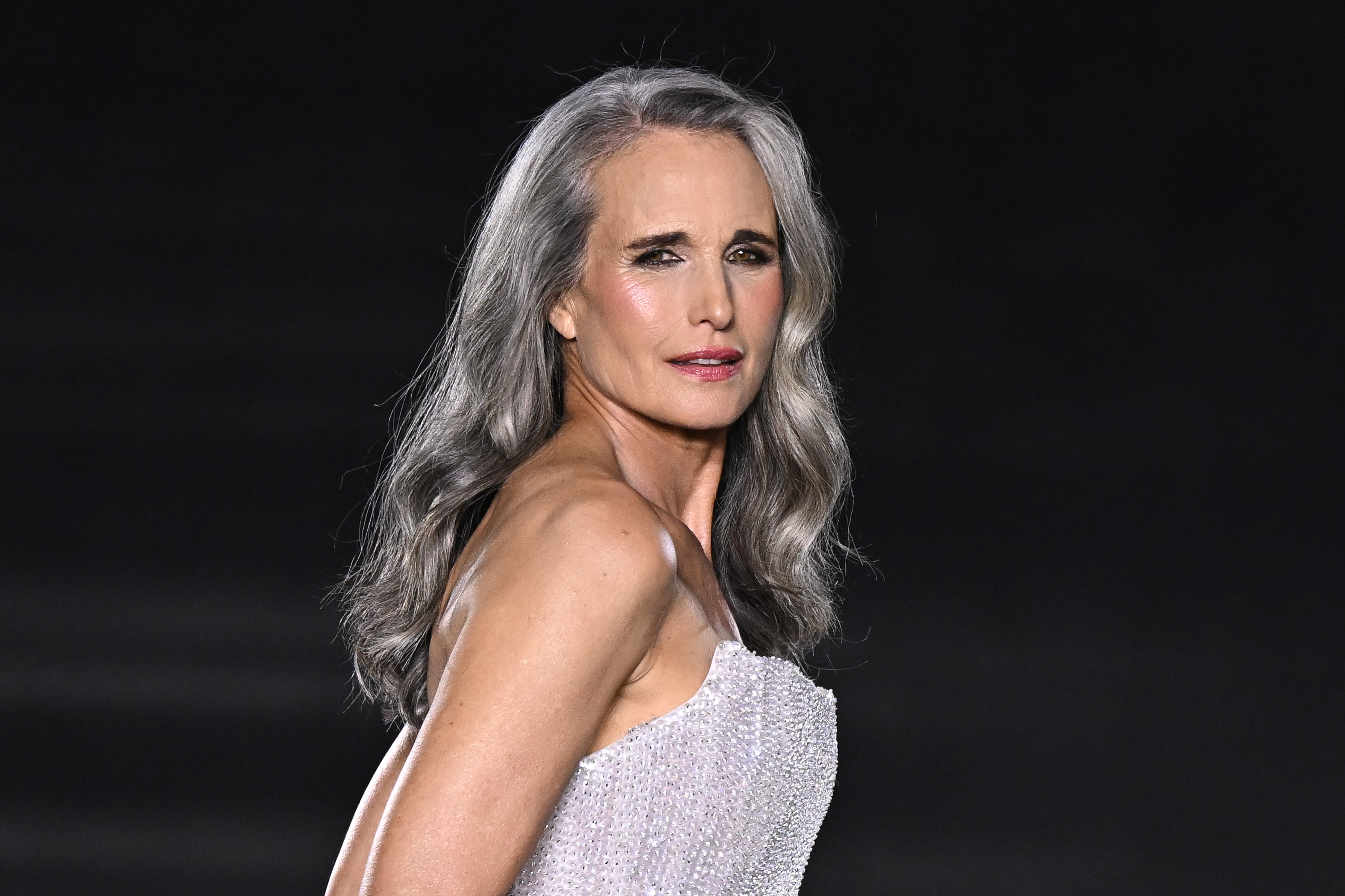 MacDowell wears her long silver hair in loose waves at the L'Oréal Paris fashion show in September 2024. Her hair had grown noticeably grayer since her 2022 Cannes appearance, showing how her natural color continued to change over time.