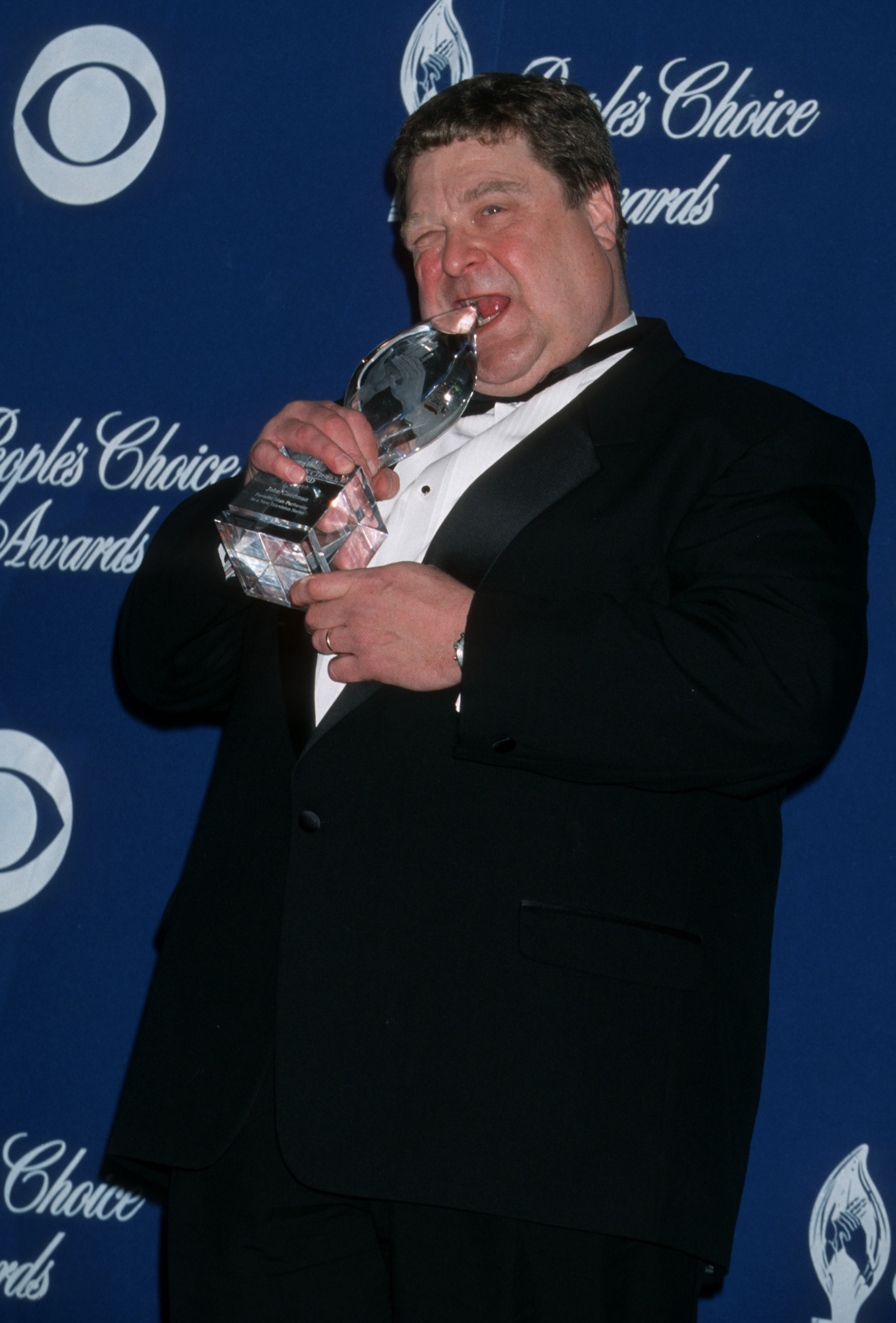 John Goodman adds a playful moment to the 2001 People’s Choice Awards by pretending to bite his trophy, showing the lighter side of the actor during the height of his fame. | Source: Getty Images