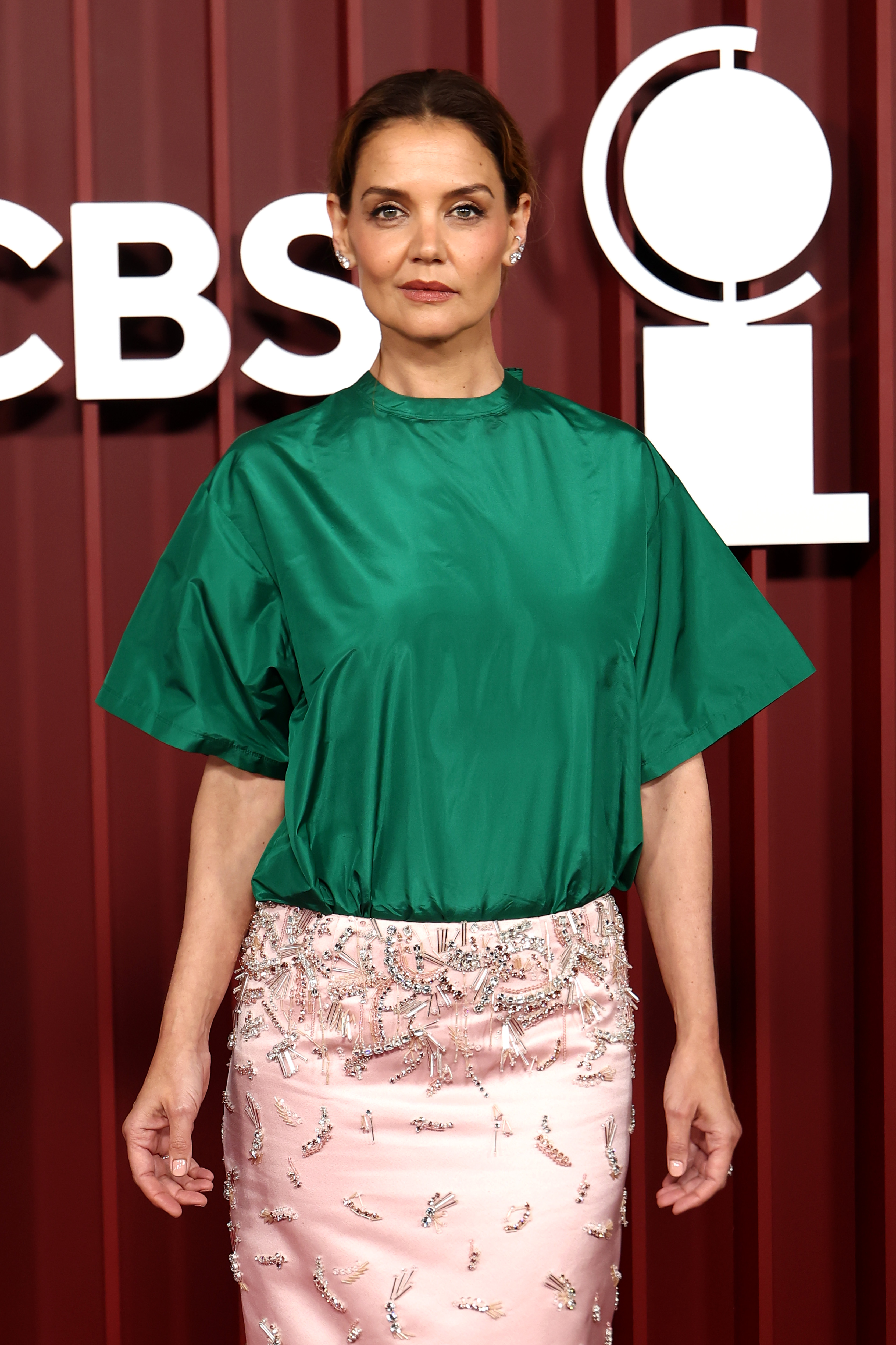 Katie Holmes poses front and center at the 78th Tony Awards in a structured green satin top and a pale pink skirt detailed with crystal embroidery. Her poised expression adds elegance to the bold color pairing at Radio City Music Hall.