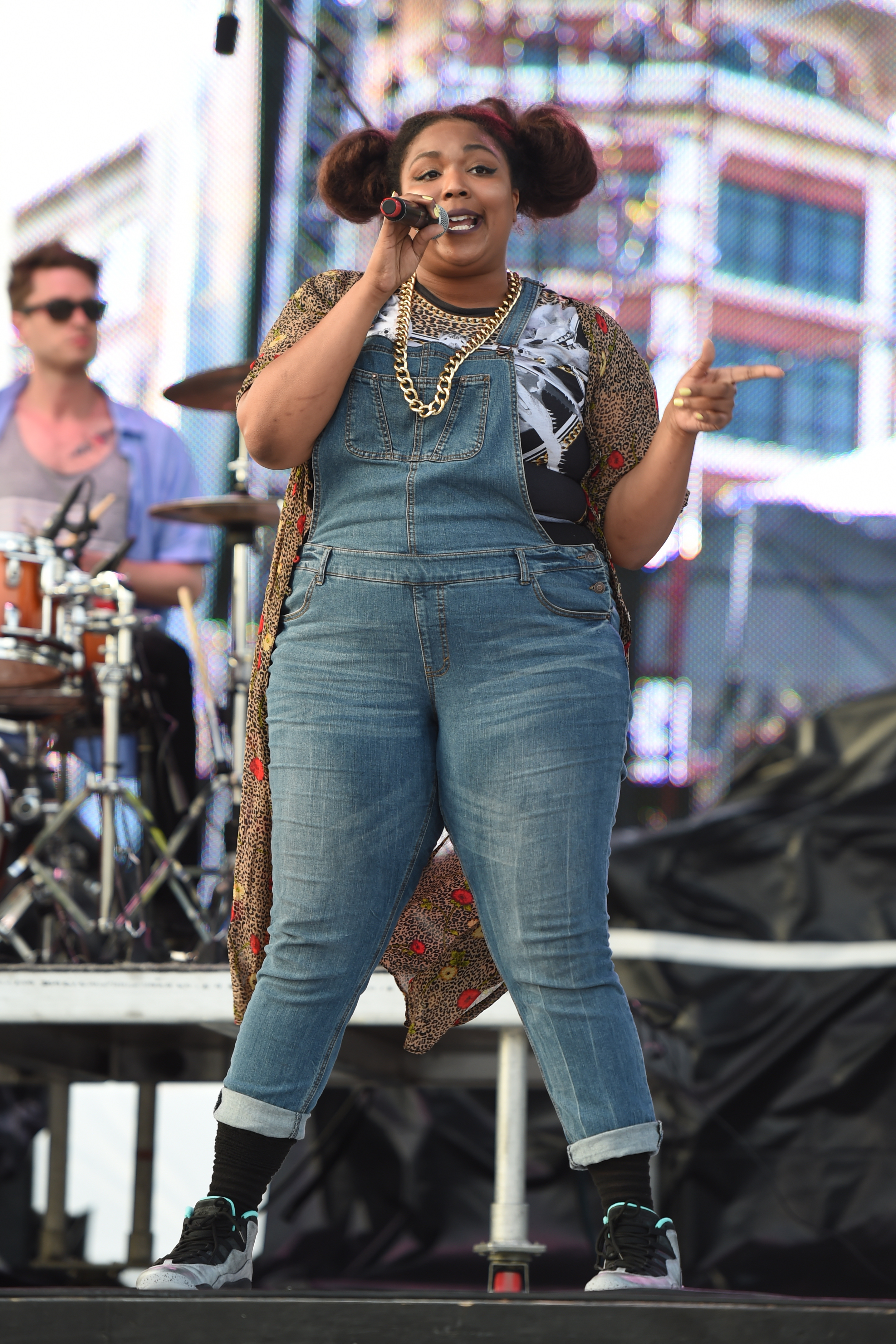 Onstage at Sunfest, Lizzo commands attention with playful confidence, gripping the mic as she begins to find her rhythm in front of a growing crowd. Dressed in denim overalls and bold styling, the moment captures an artist still rising — raw, vibrant, and already impossible to ignore.