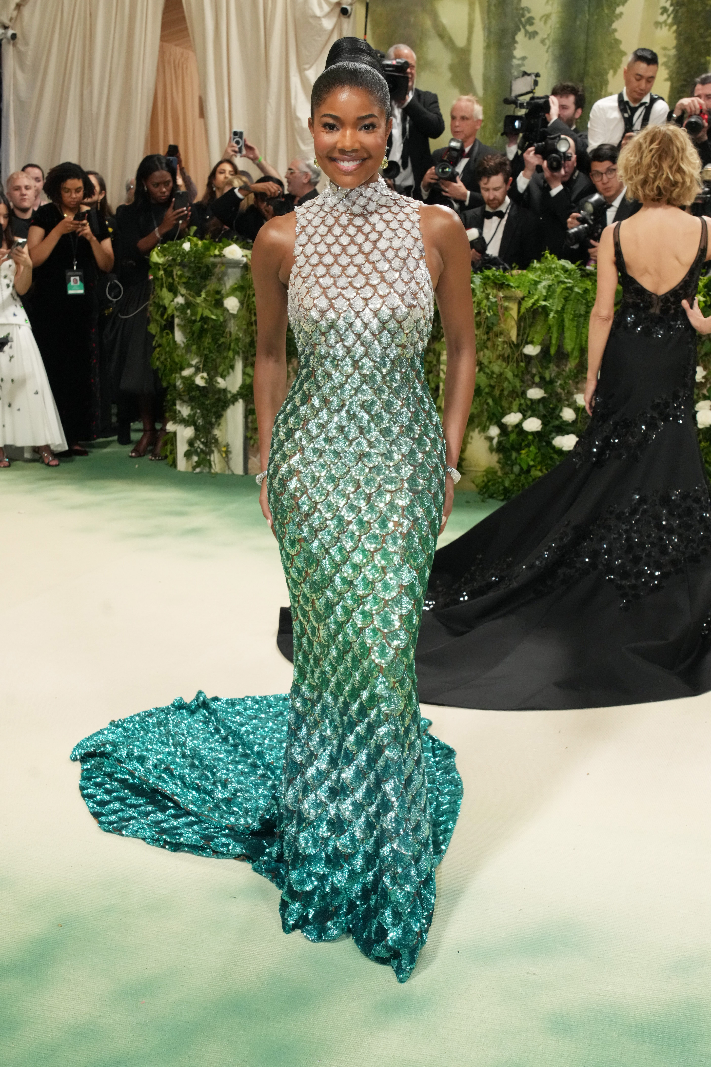 Gabrielle Union dazzles on a red carpet in a shimmering, scale-patterned gown that transitions from silver at the top to emerald green at the bottom. | Source: Getty Images