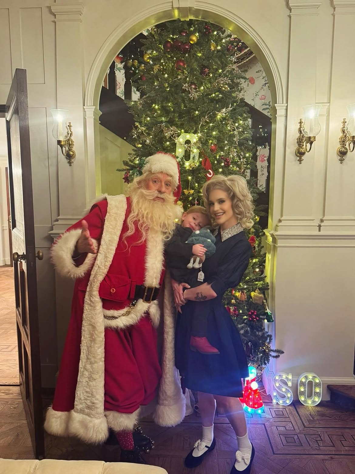 Kelly Osbourne held her son Sidney, who clutched a blue stuffed dinosaur, beside a towering Christmas tree during the family's first holiday season without Ozzy. | Source: Instagram/@kellyosbourne