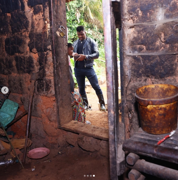 A photograph taken from inside a dim brick structure showed Francis Ngannou standing beyond the doorway in the daylight while household items, including a worn container, were visible in the foreground. The image was among those from his Batié visit that later drew attention online, with some commenters focusing on the living conditions shown in the photographs and questioning why they appeared modest despite Ngannou's success as a champion. | Source: Instagram/francisngannou