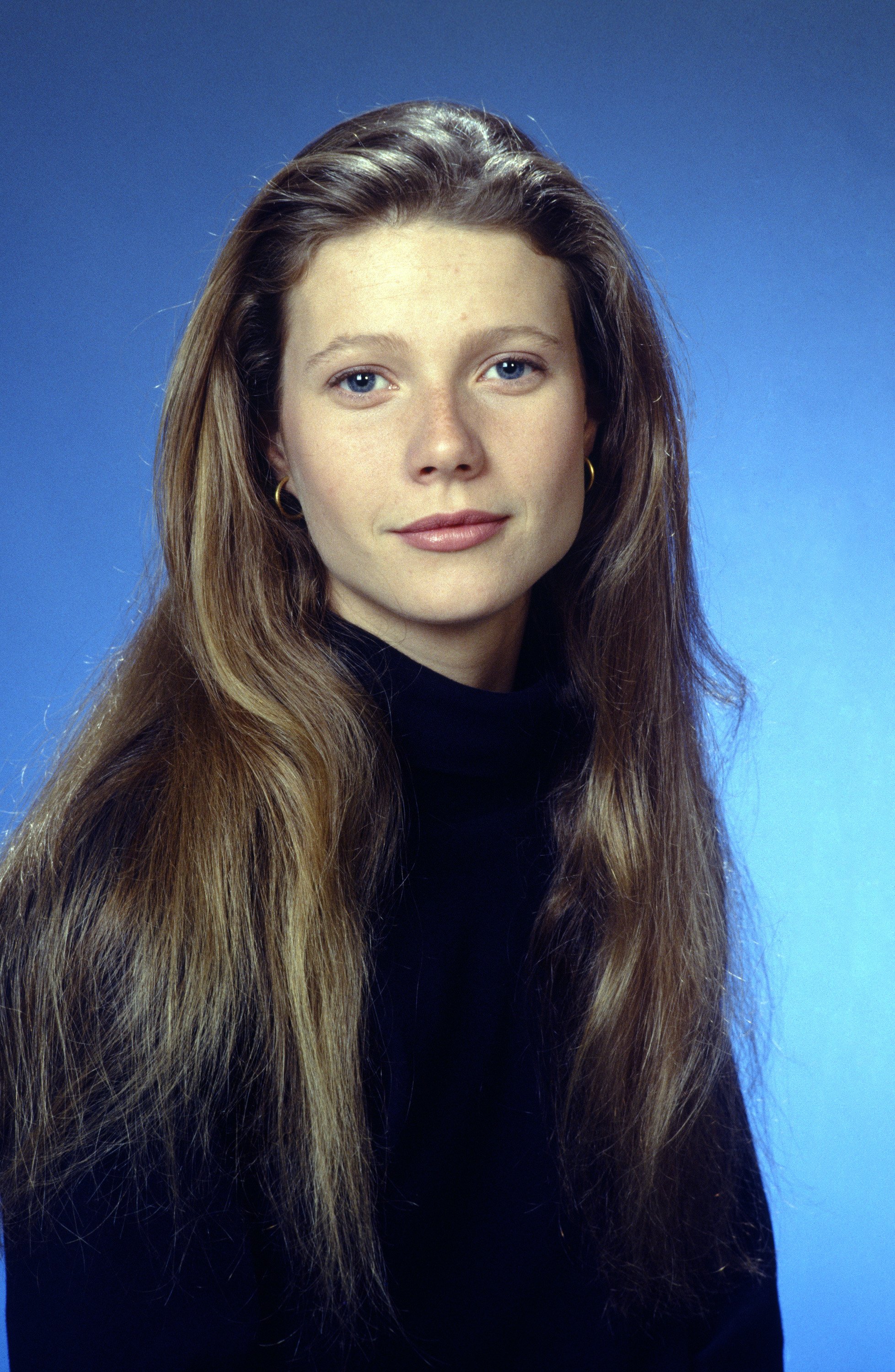 Gwyneth Paltrow appears in 1992 as Angela Pritchard in “Cruel Doubt,” with her long, light brown hair parted down the middle and flowing naturally over her shoulders. She wears a simple black turtleneck and small gold hoop earrings, her fresh complexion and soft makeup accentuating her youthful, delicate features.
