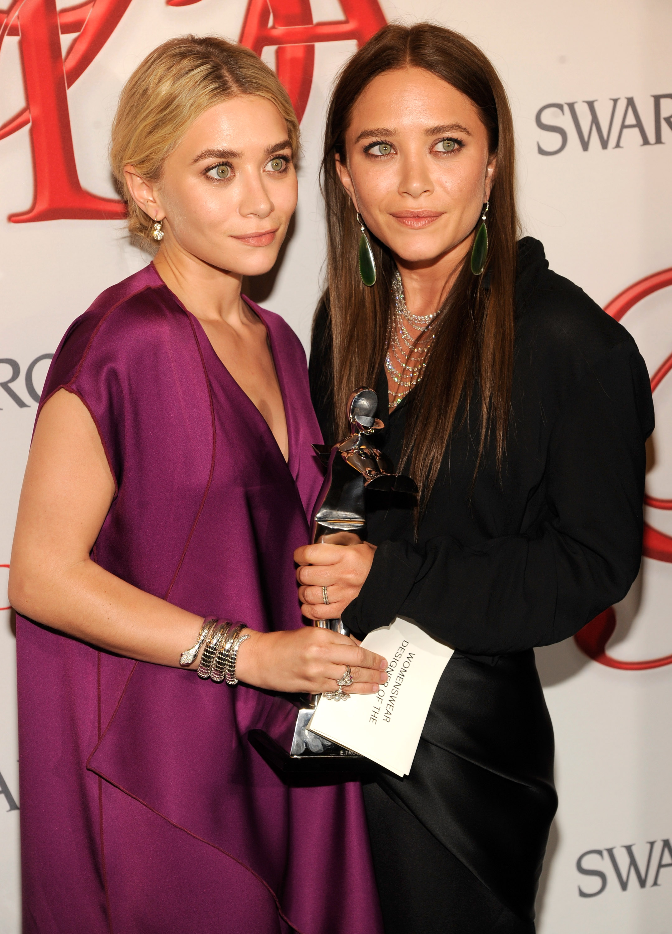 Strikingly mature bone structure and sleek, center-parted hairstyles defined 26-year-old Mary-Kate and Ashley Olsen at the CFDA Fashion Awards on June 4, 2012, where Ashley wore a deep purple draped gown with stacked silver bracelets and Mary-Kate opted for a black blouse with long, straight dark-blonde locks and statement drop earrings.